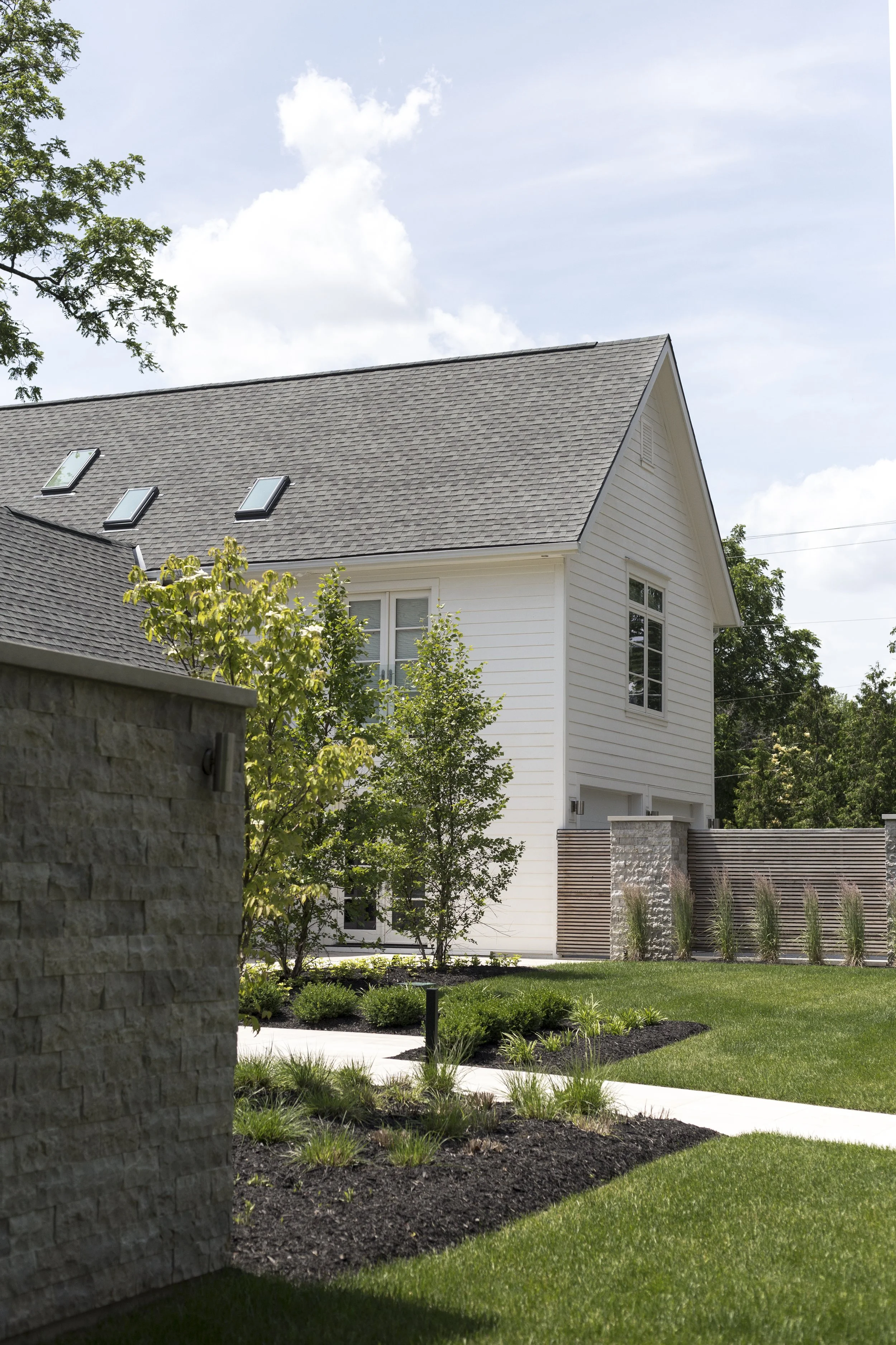 A white two-story house with a gable roof, windows, and a backyard with trees, shrubs, grass, and a wooden fence.