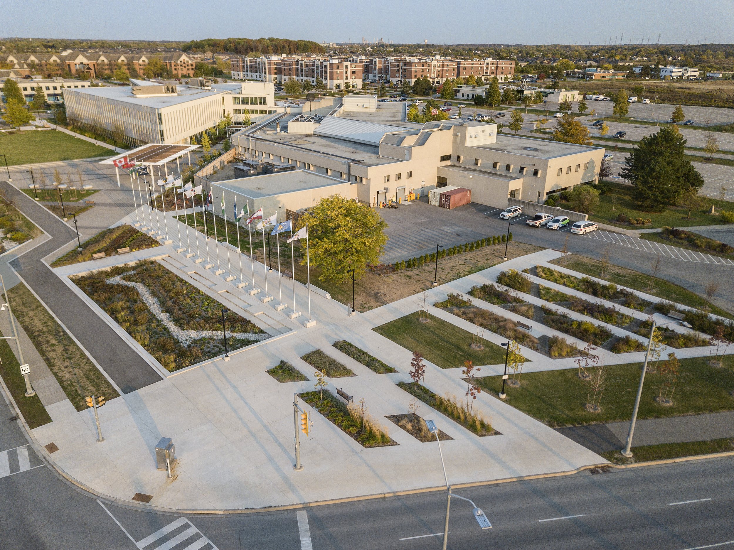 Aerial view of a modern municipal building with a landscaped garden, flagpoles, and parking lot in an urban area.