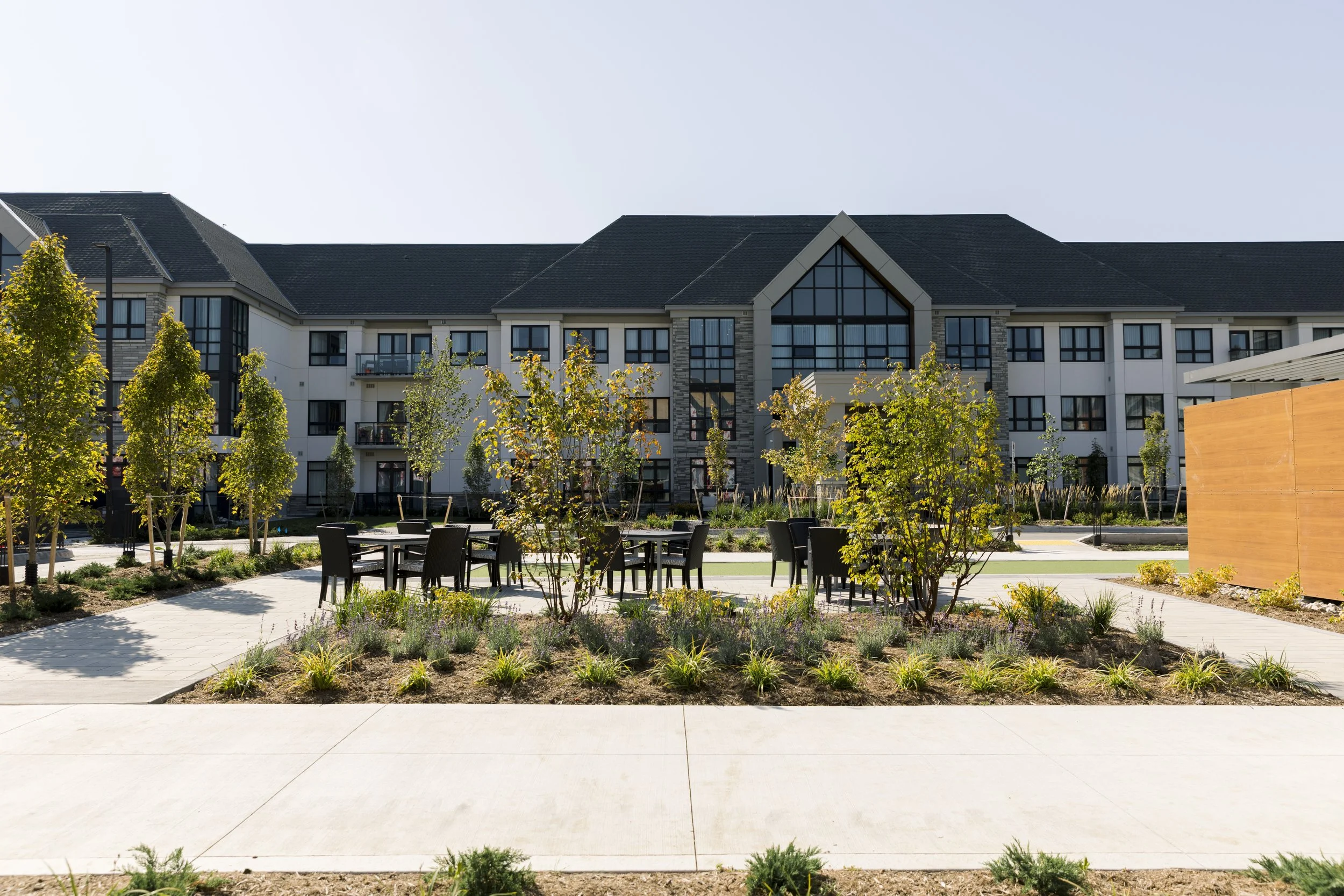 Modern apartment complex with landscaped courtyard featuring trees, plants, and outdoor seating areas.
