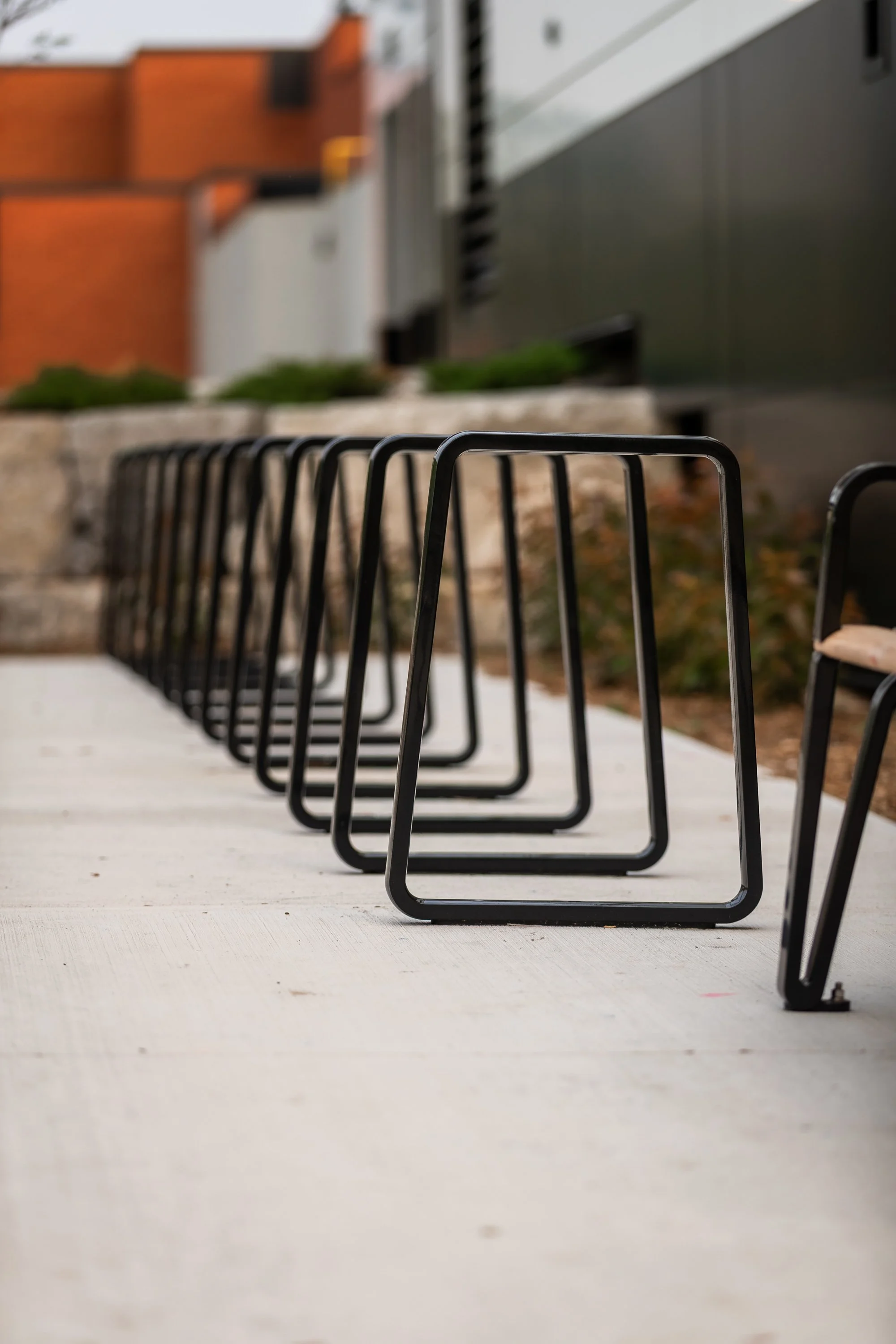 Several black metal chairs arranged in a row outdoors on a concrete surface.