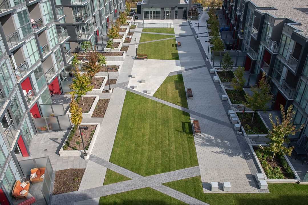 Aerial view of a modern urban apartment complex with landscaped courtyard, sidewalks, benches, and trees.