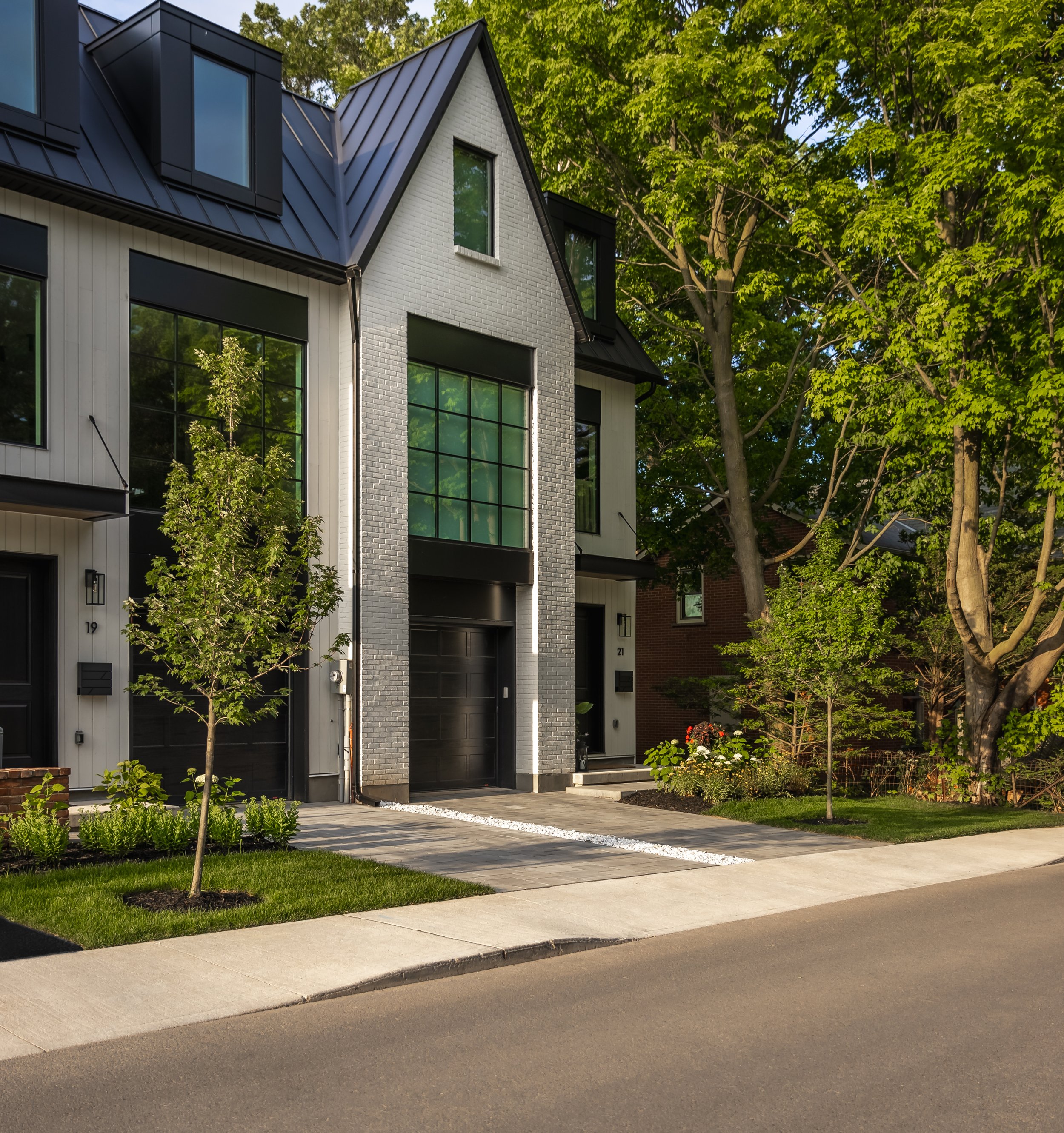 Modern townhouse with large windows, black garage door, and modern landscaping, surrounded by trees and greenery.