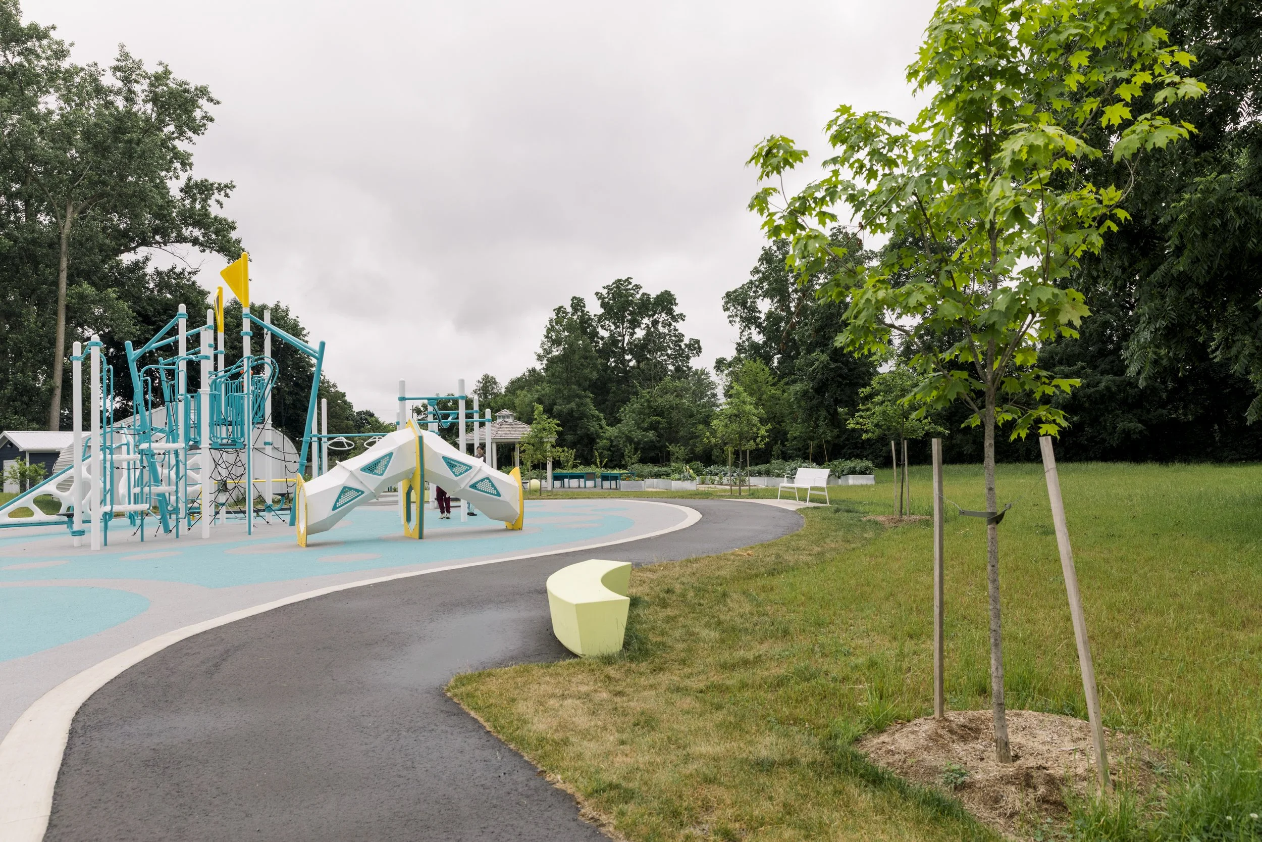 Empty playground with colorful play structures and surrounding trees on an overcast day.