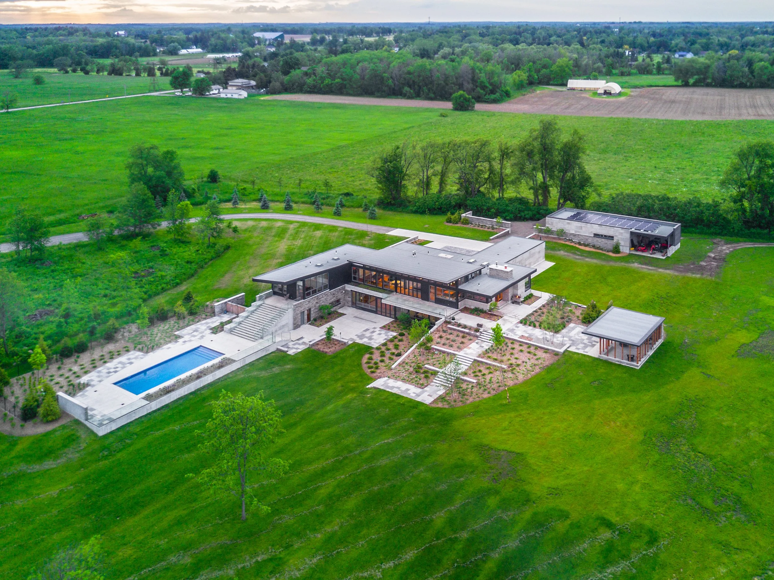 Aerial view of a modern house with a swimming pool, landscaped yard, and surrounding green fields.