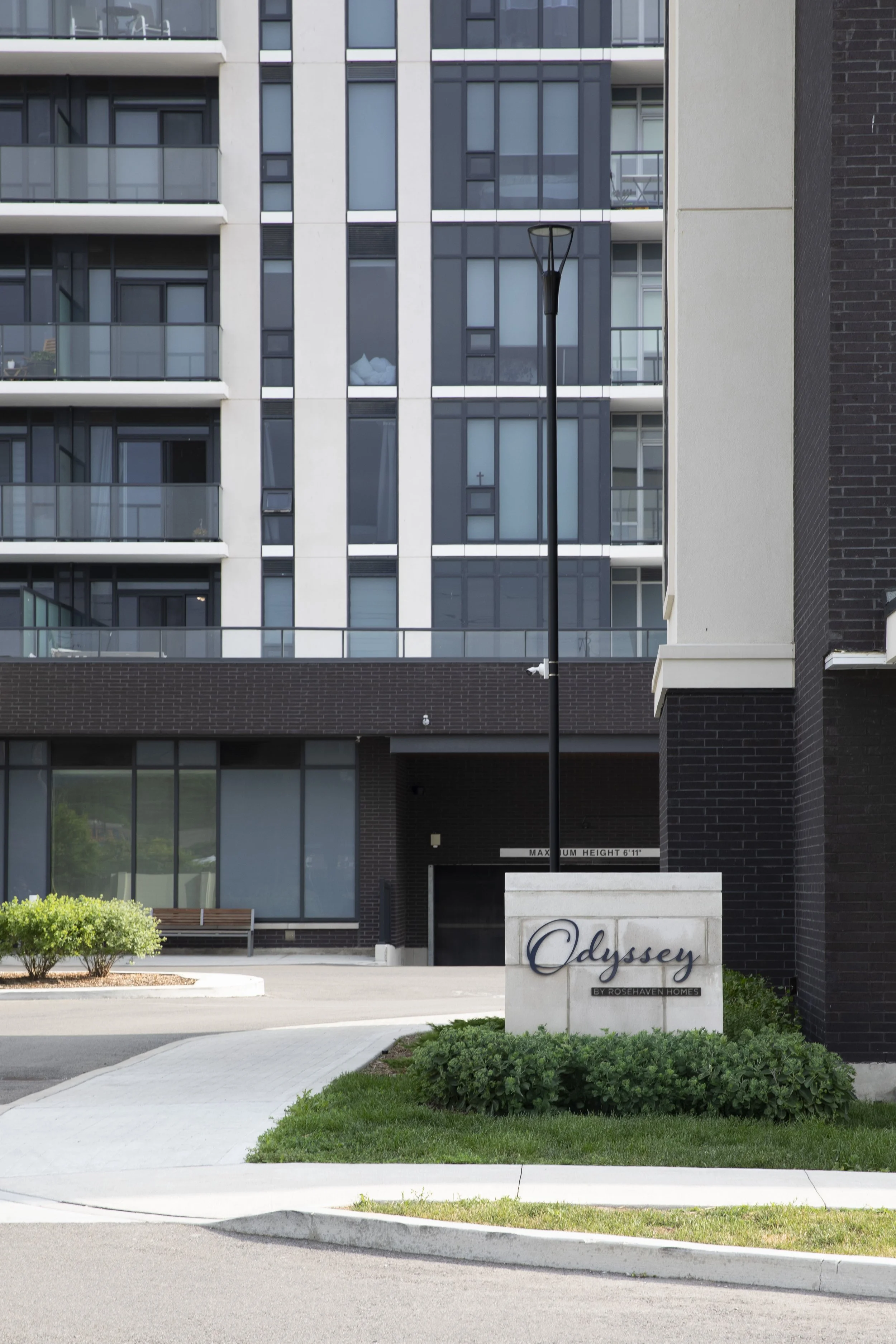 Apartment building with a sign that reads 'Odyssey' near the entrance, landscaped with bushes and a sidewalk.
