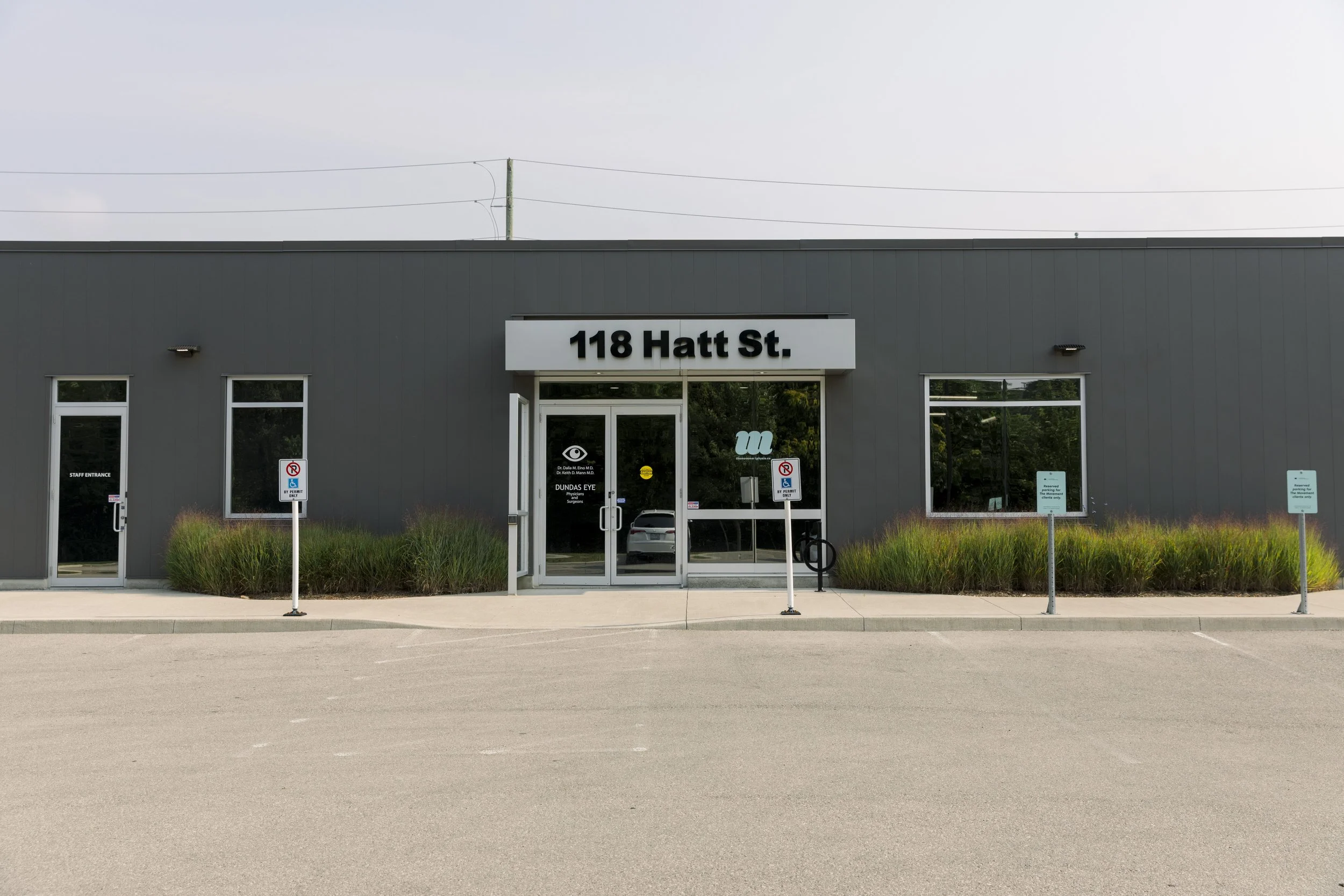 A modern gray commercial building with a sign that reads '118 Hatt St.' above the entrance, surrounded by a parking lot and landscaping, with no cars parked and no people visible.