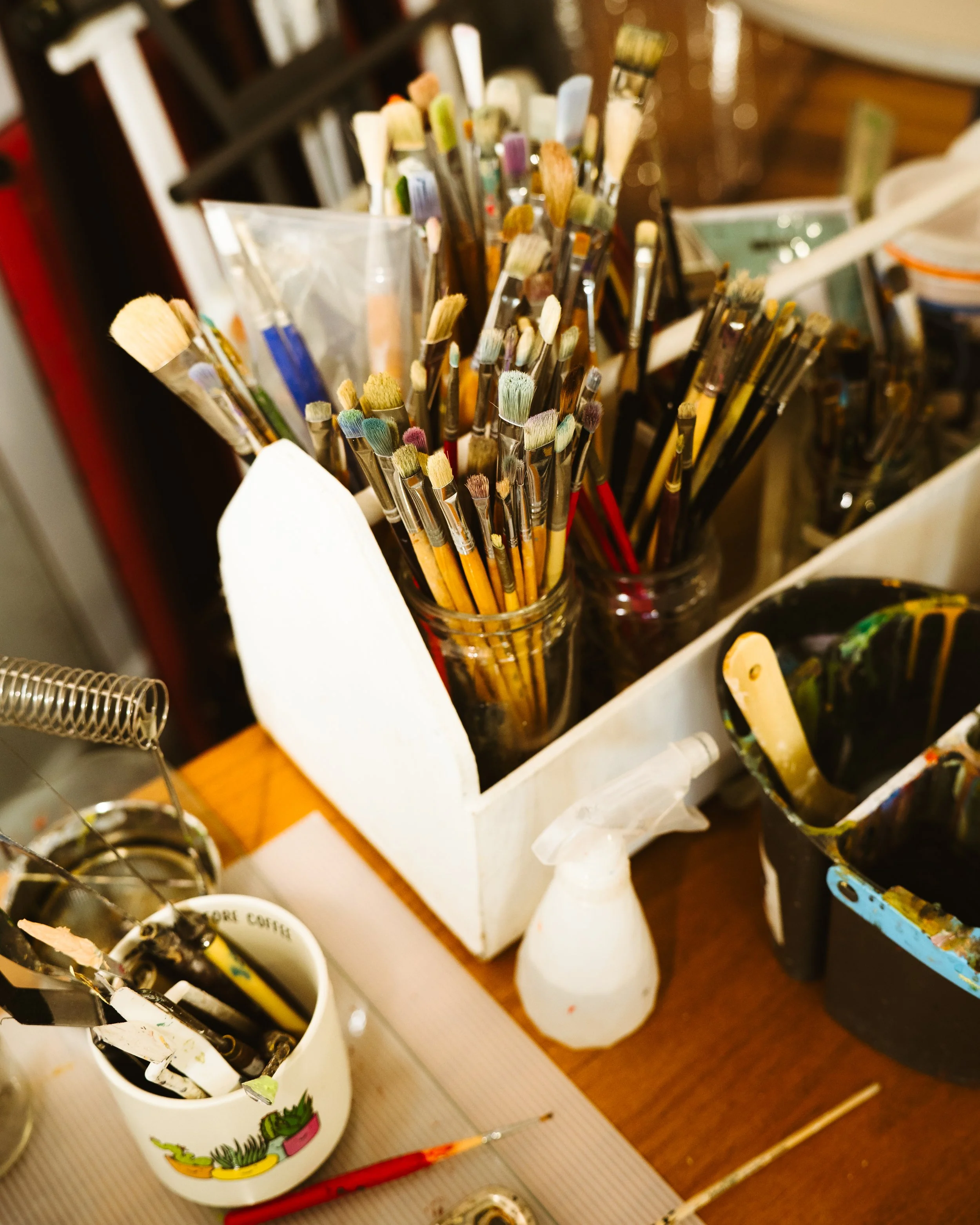 A workspace with paintbrushes in glass jars, a spray bottle, and various painting supplies.