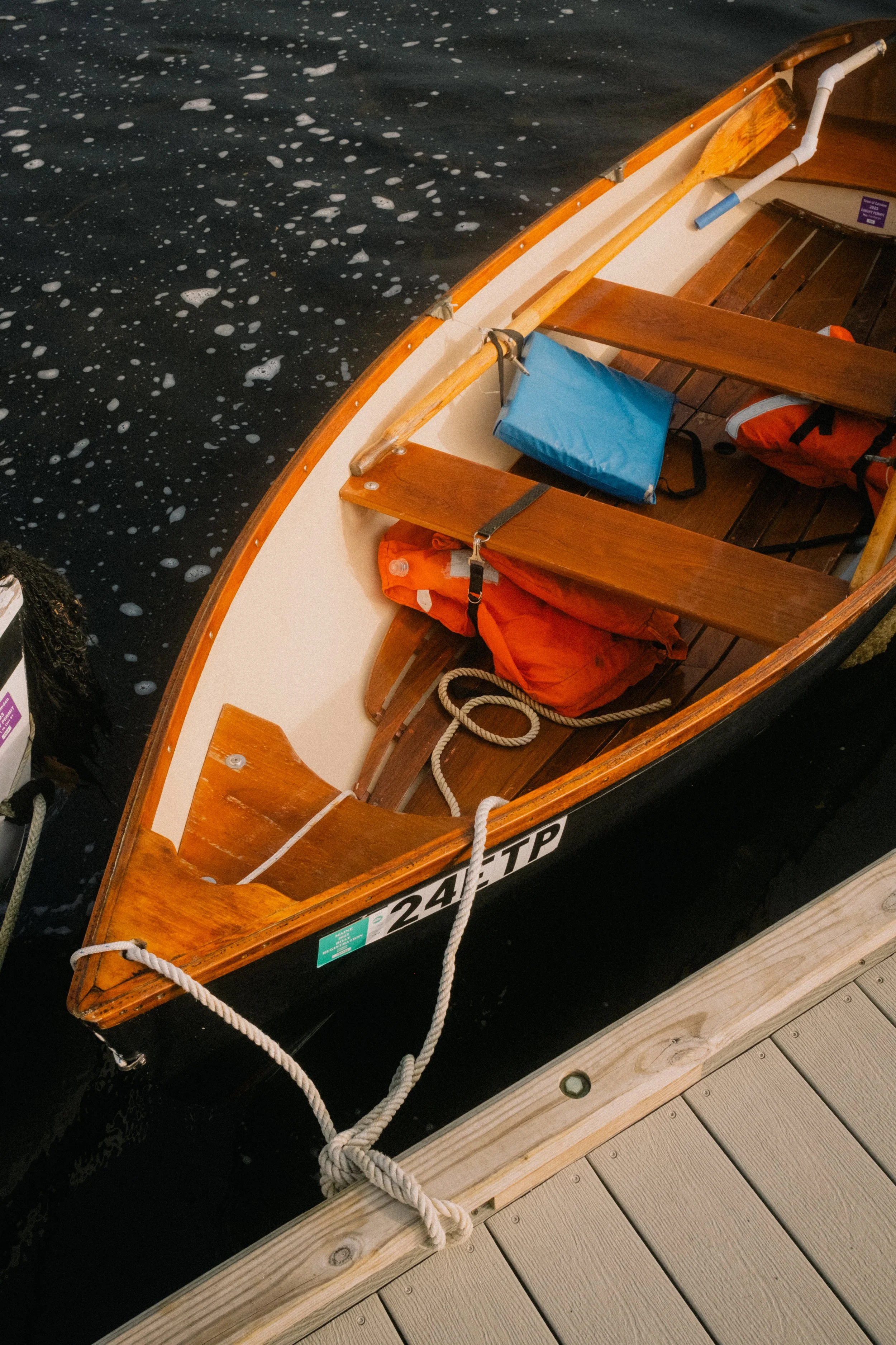 A wooden rowboat tied to a dock, with life jackets and a blue bag inside. Camden, Maine. Virginia Travel Photographer.