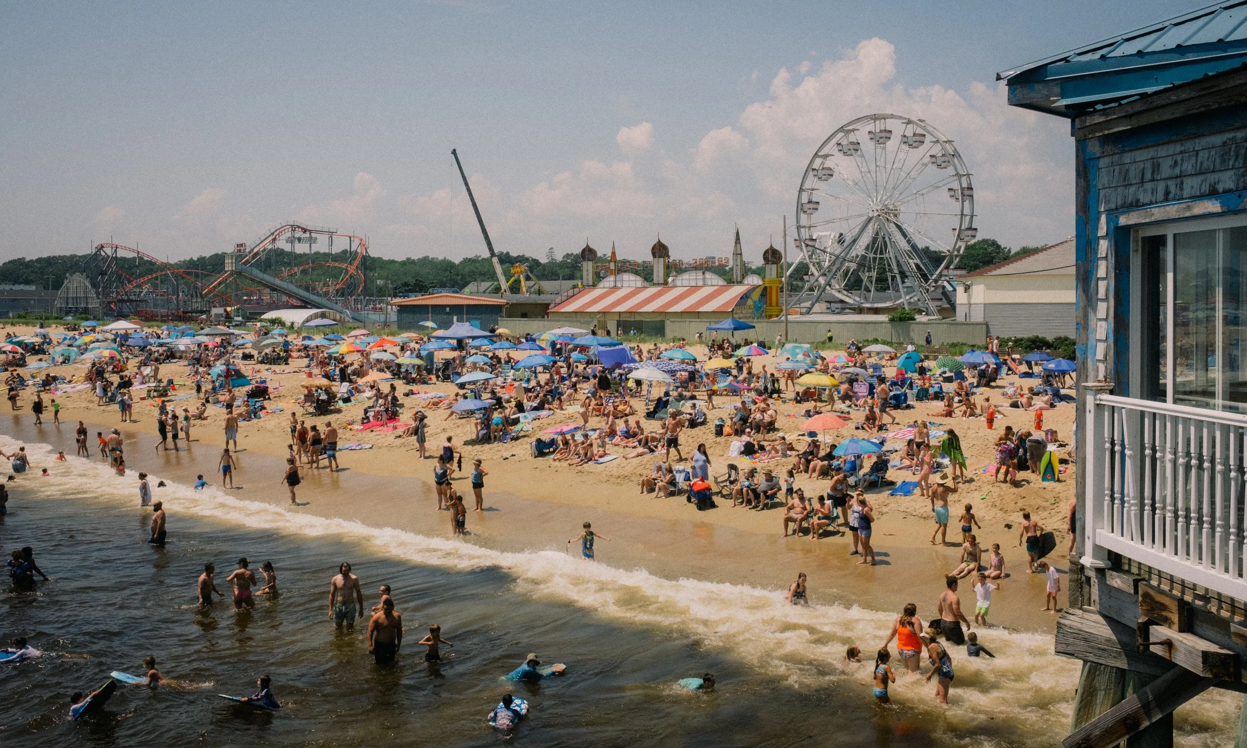 Old Orchard Beach, Maine. Virginia Travel Photographer. Beach with many people, umbrellas, and children in the water near an amusement park with a roller coaster, Ferris wheel, and colorful tents.