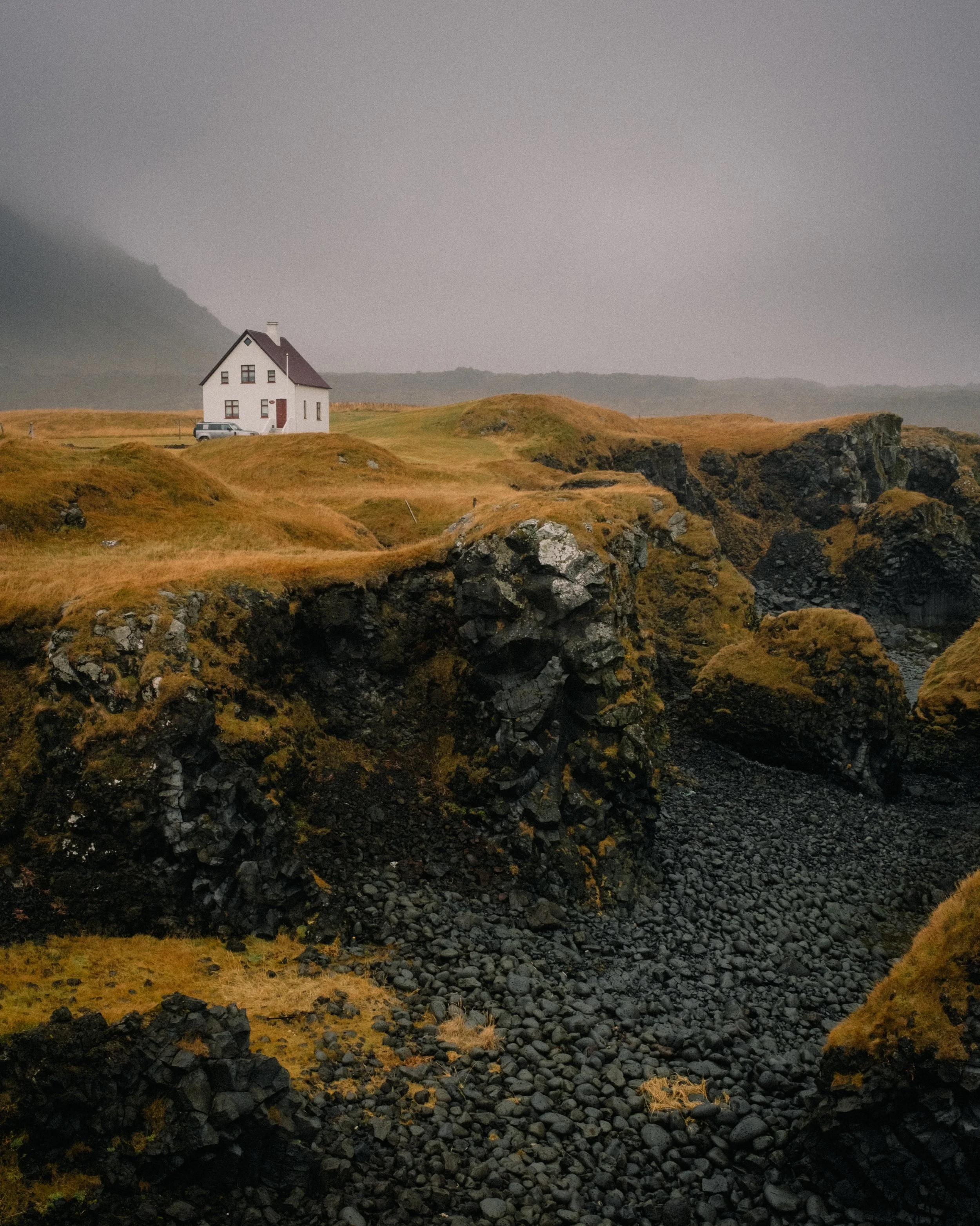 Iceland. A white house with a red roof on a grassy hill overlooking a rocky canyon under an overcast sky. Virginia Travel Photographer. 