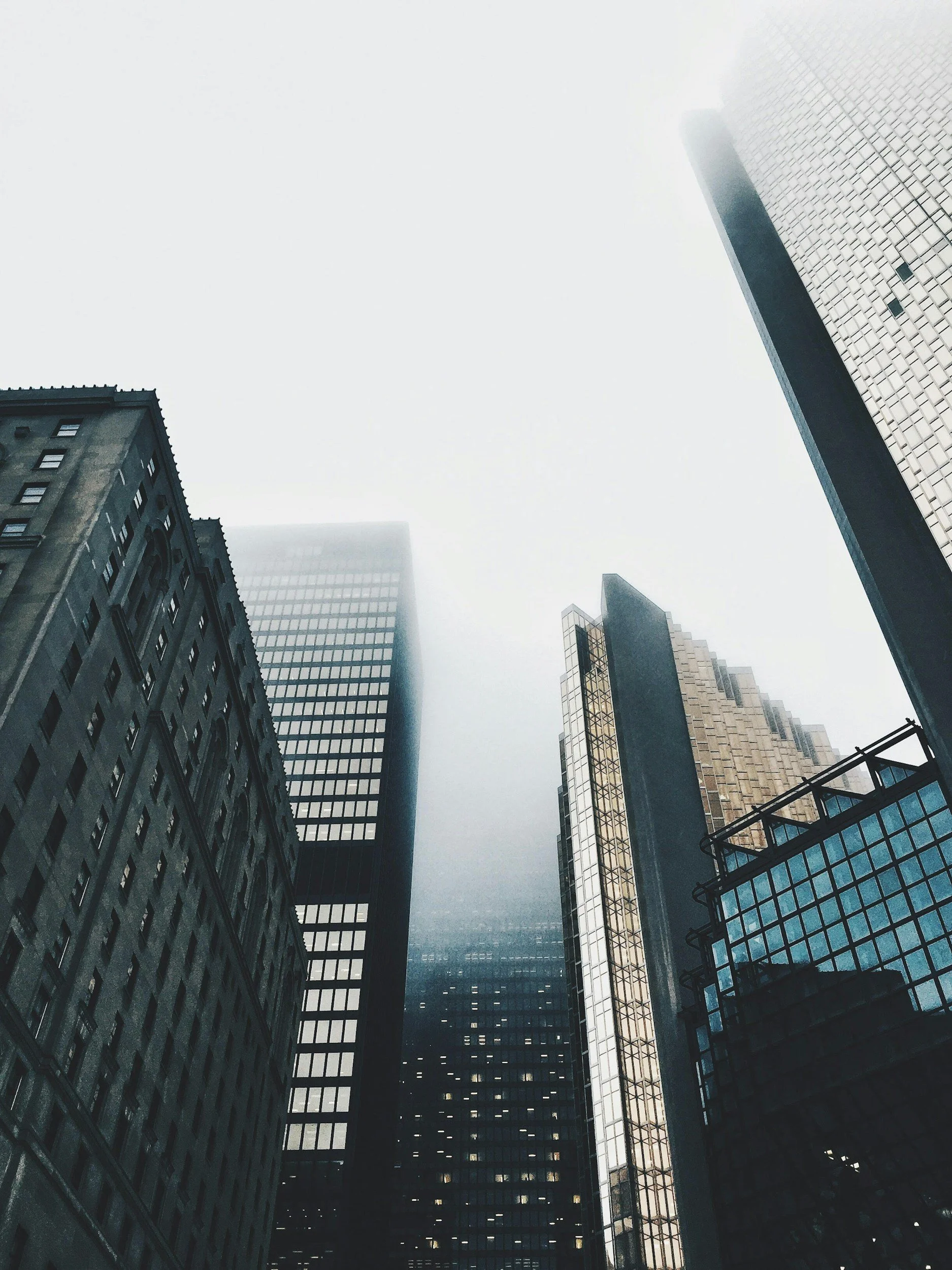 Looking up at tall skyscrapers in a city with fog and cloudy sky