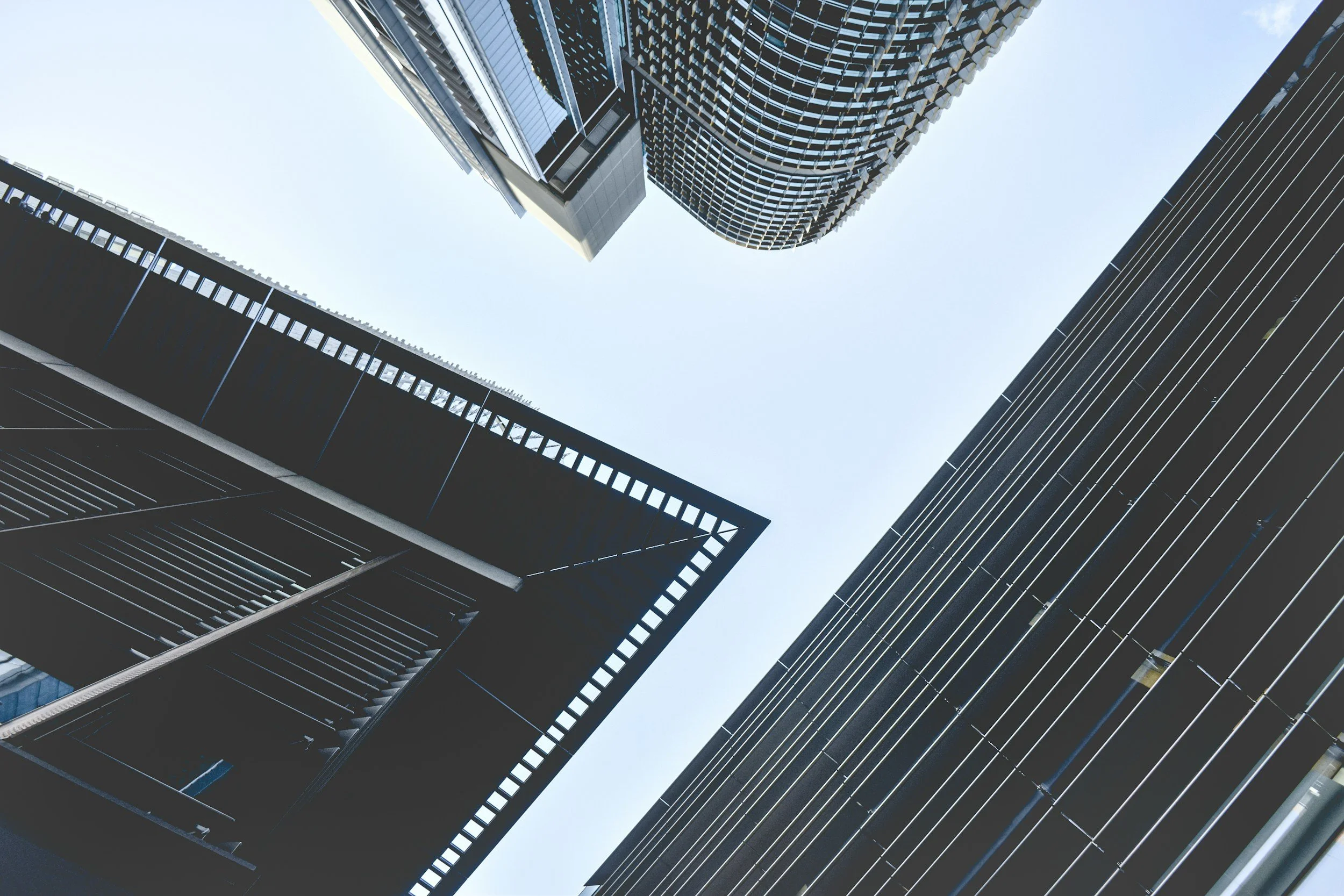 Looking up at a cluster of modern skyscrapers with glass facades and a clear blue sky.