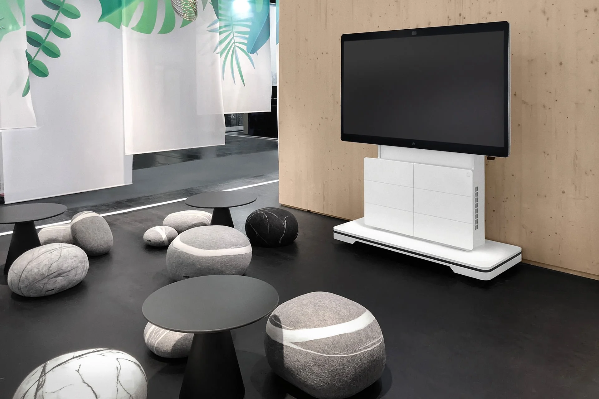 Moderner Innenraum mit schwarzen Tischen, Steinen und einem großen Bildschirm an einer Holzwand.