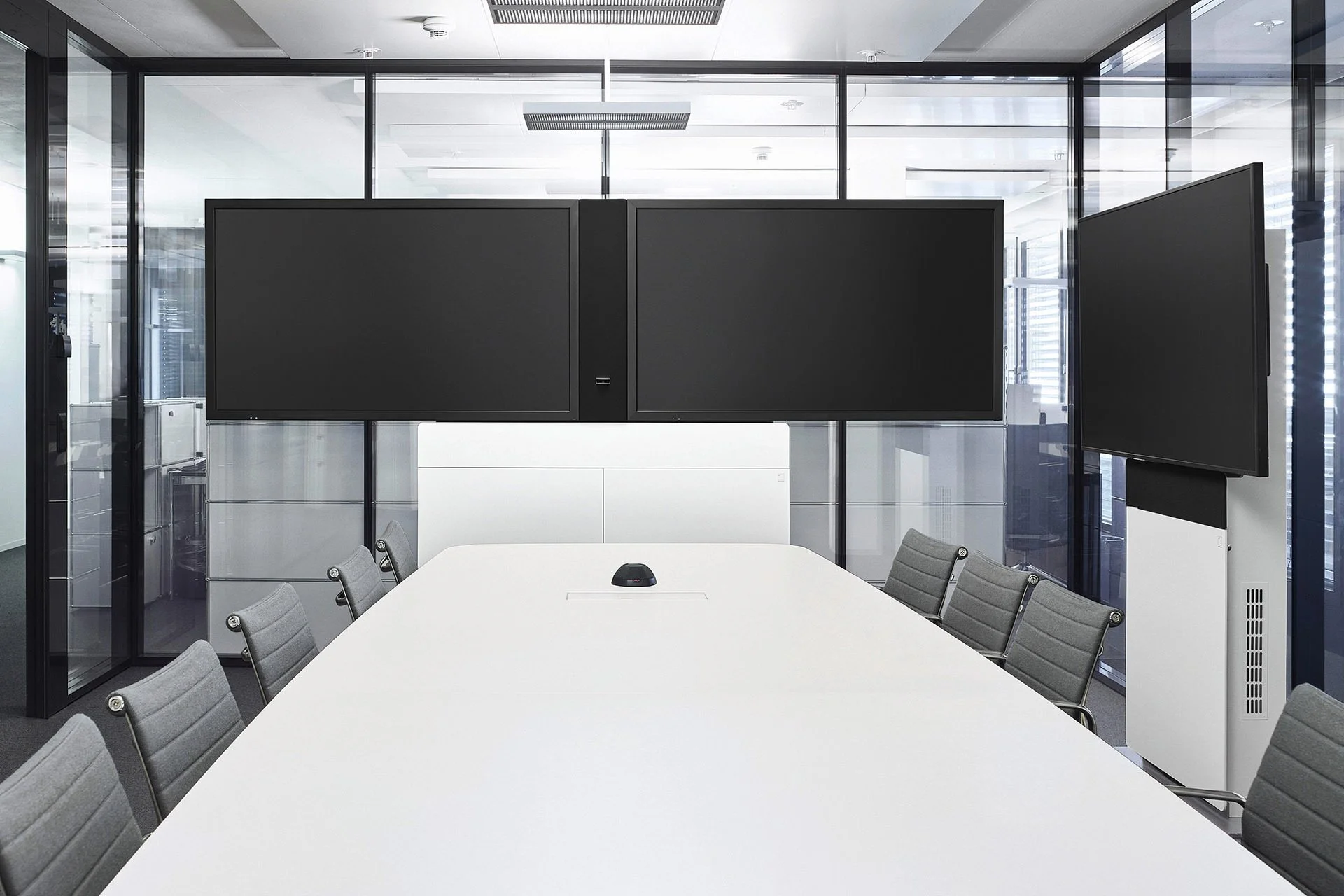 Leere moderne Konferenzraum mit weißen Tisch, schwarzen Bildschirmen und grauen Stühlen.