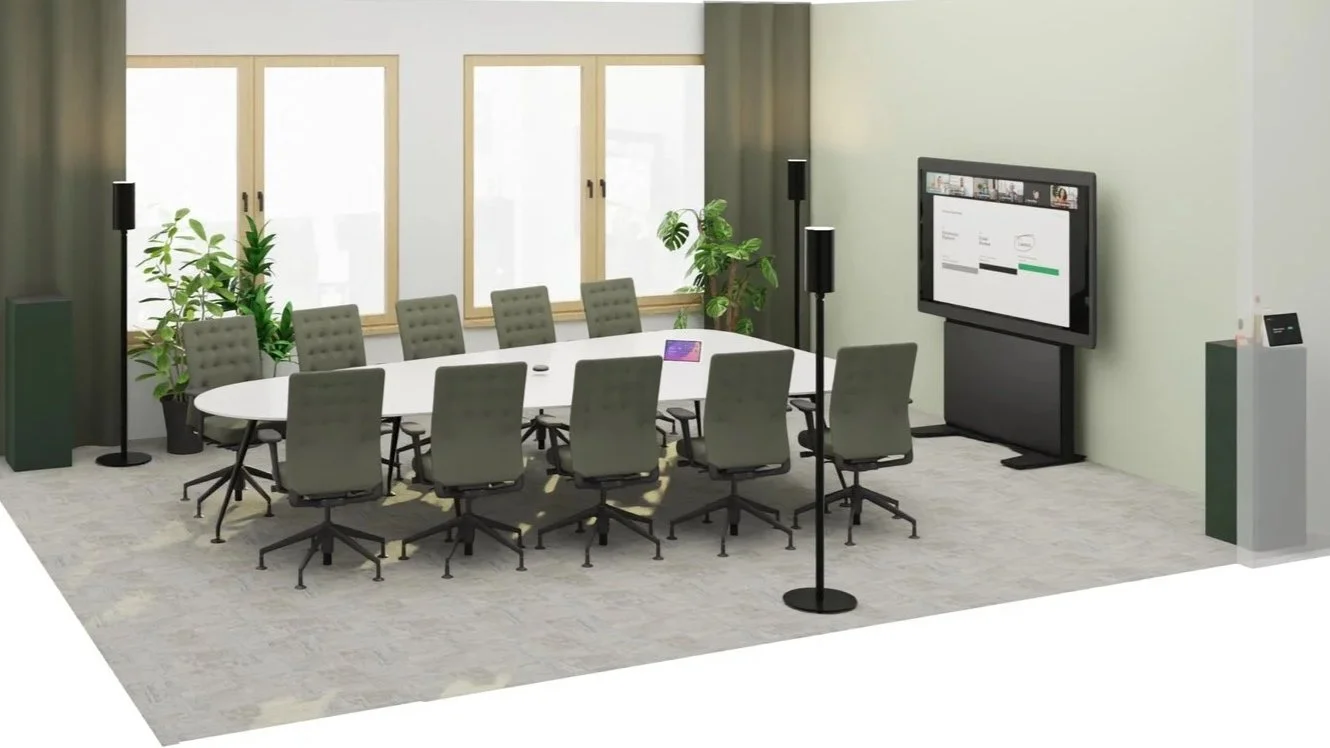 Ein Konferenzraum mit einem ovalen Tisch, mehreren Stühlen, Pflanzen, einem großen Bildschirm und einer Kamera auf einem Stativ.