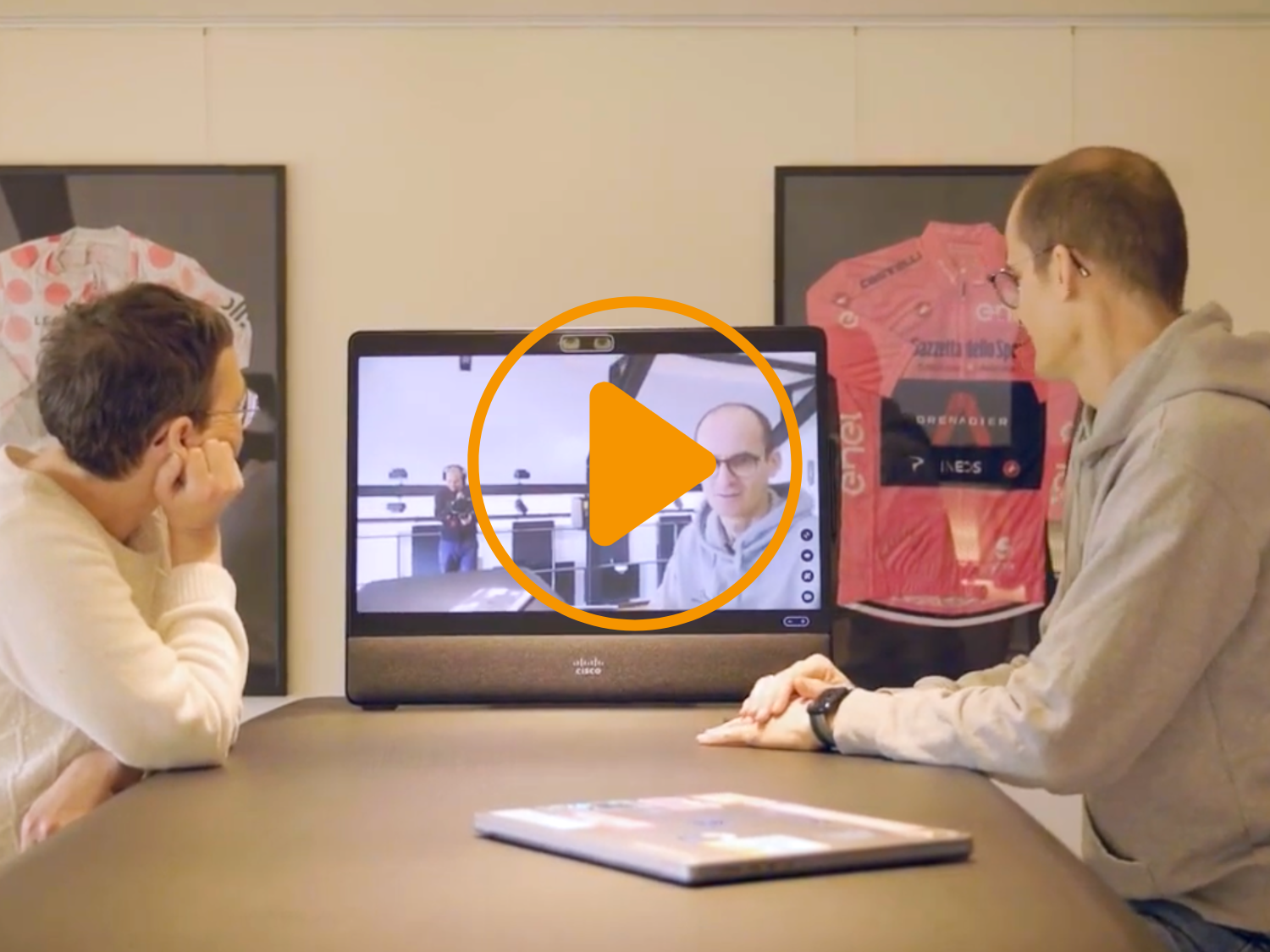 Eine Frau und ein Mann sitzen an einem Tisch und schauen auf eine Cisco Desk Pro G2