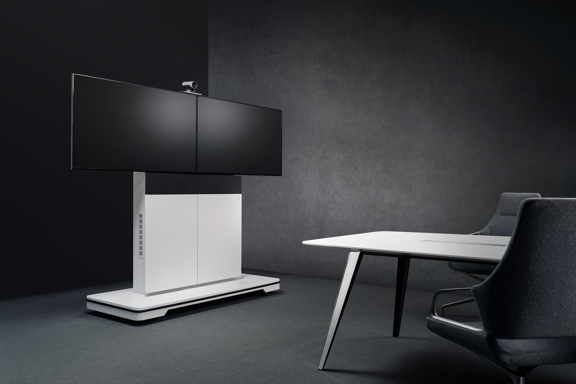 Ein moderner, minimalistischer Konferenzraum mit dunklen Wänden, einem weißen Tisch mit schwarzen Beinen, einem schwarzen Chefstuhl und einem großen schwarzen Bildschirm auf einem weißen Standfuß.