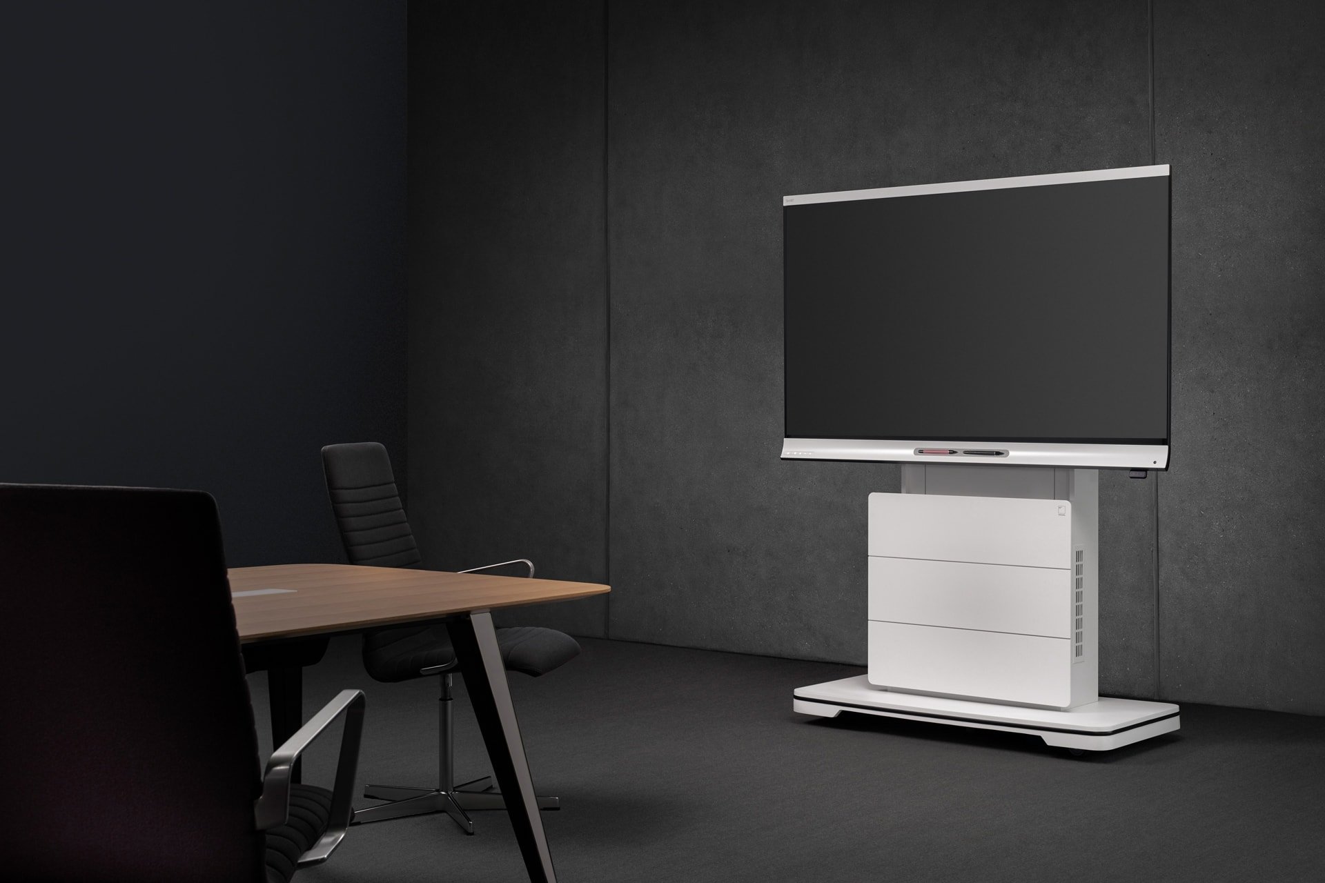 Ein dunkler Besprechungsraum mit einem modernen Whiteboard auf einem mobilen Rollständer, umgeben von schwarzen Bürostühlen und einem rechteckigen Holztisch.