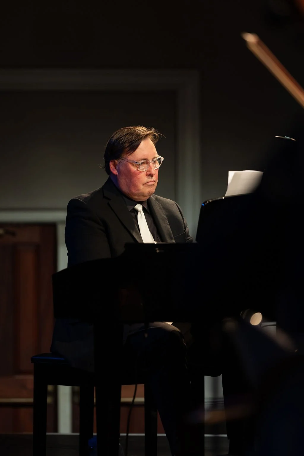 Man in a suit and tie playing the piano on stage.
