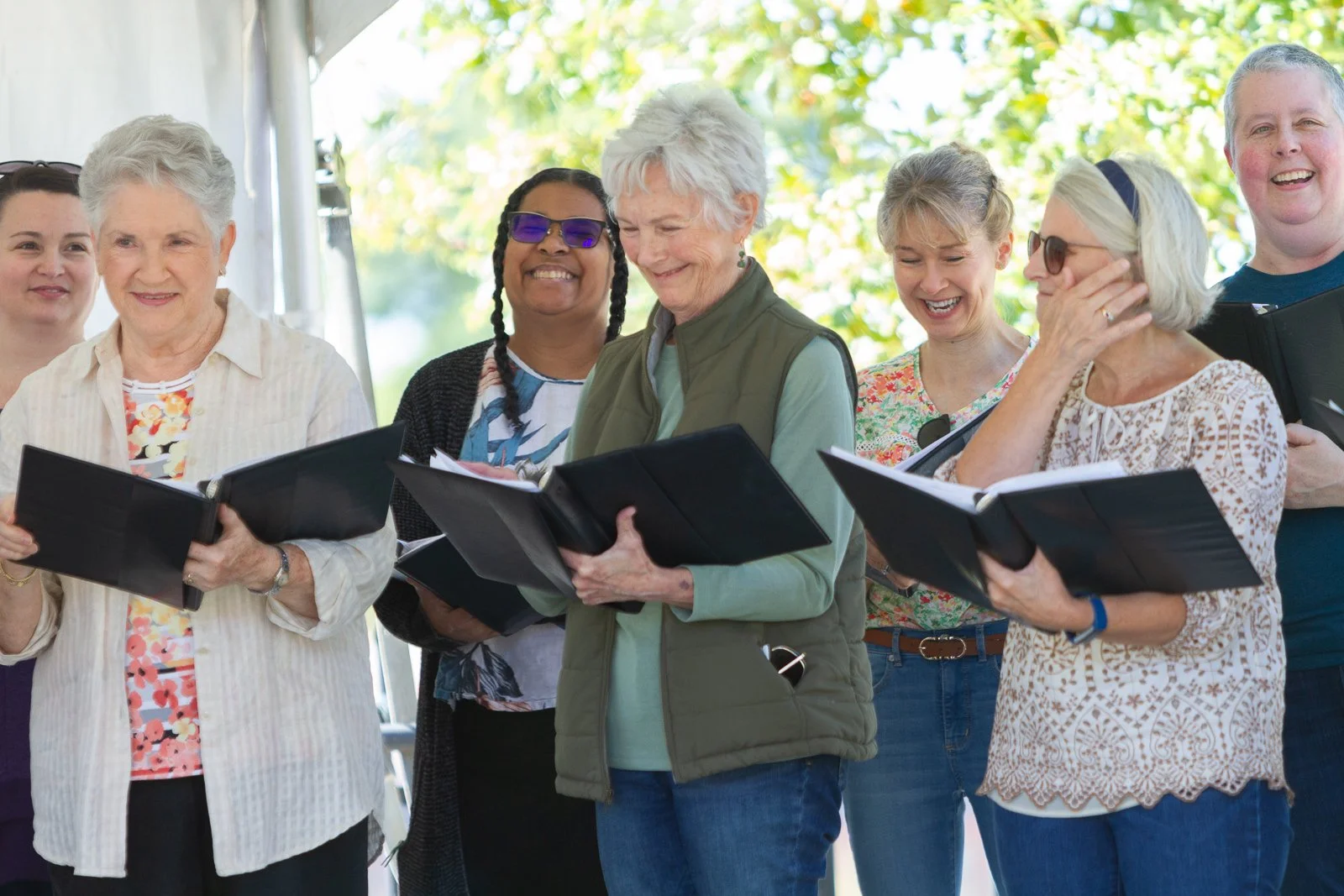 Group of women singing or reading from songbooks at an outdoor event.
