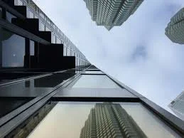 Looking up at tall skyscrapers from the ground, showing the building exteriors and partly cloudy sky.