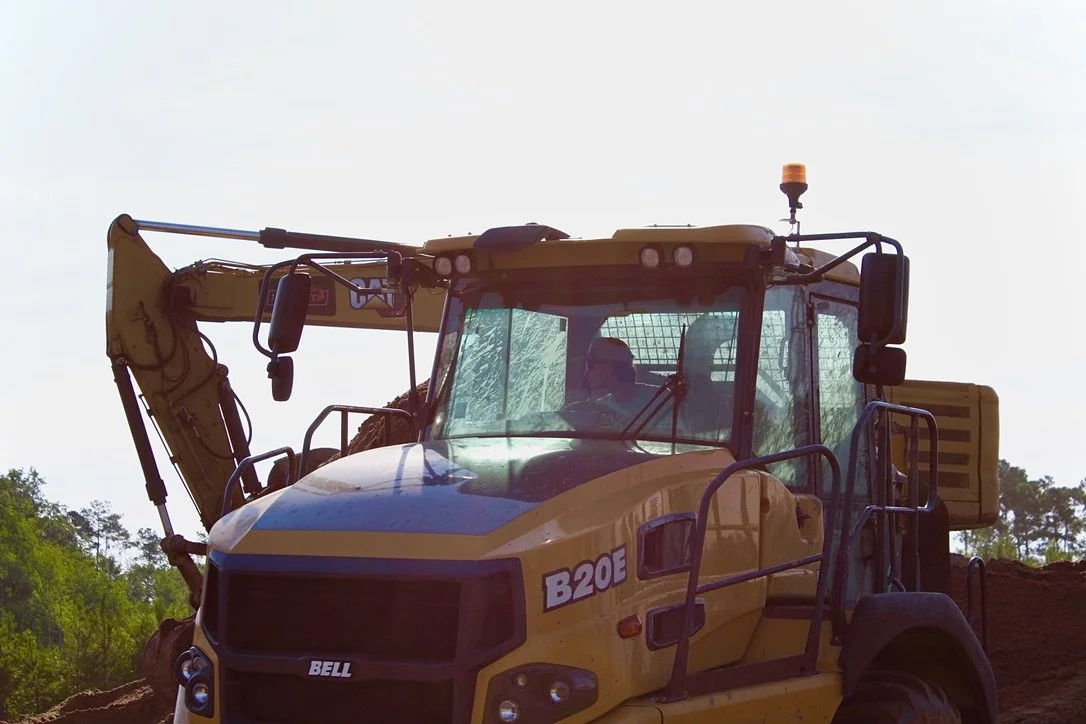 A yellow excavator machine operating on a construction site with trees in the background.