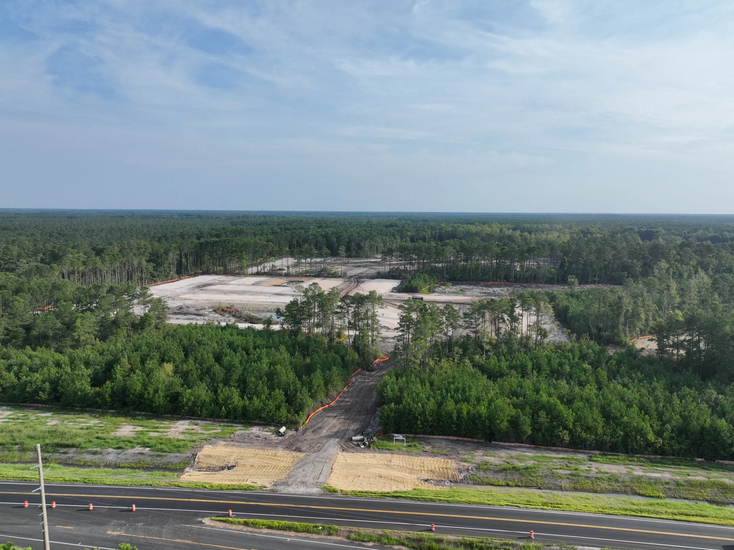 Aerial view of a forested area with construction site and land development in progress. Clear blue sky with some clouds.