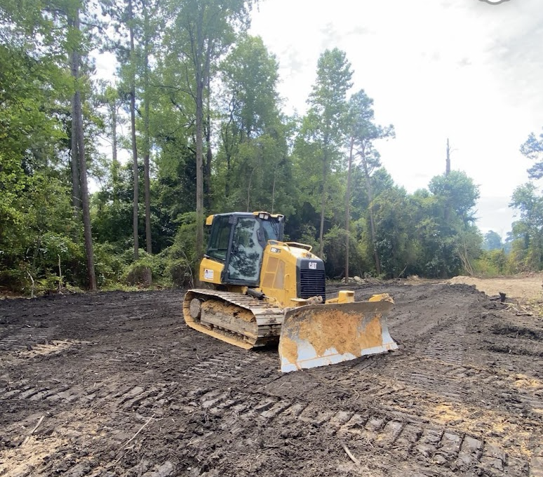 A yellow Caterpillar bulldozer on a dirt clearing surrounded by trees.