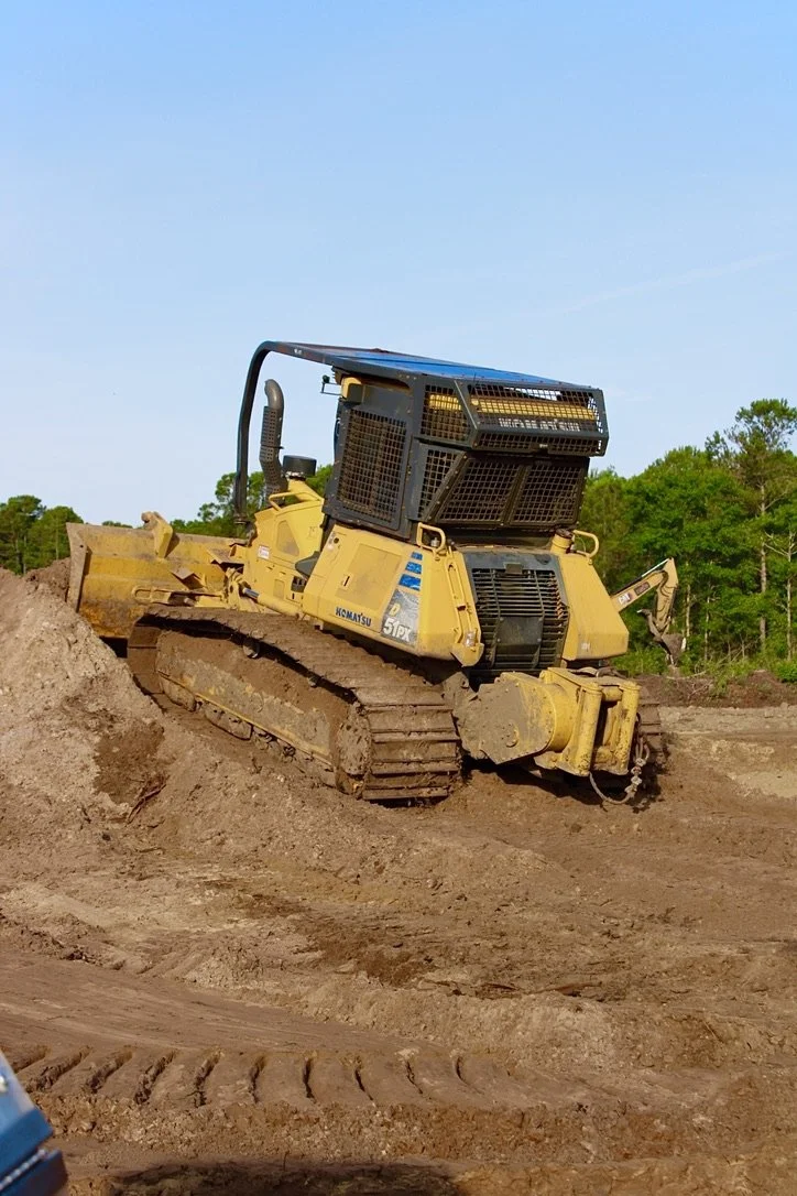 A yellow bulldozer working on a dirt construction site with trees and a blue sky in the background.