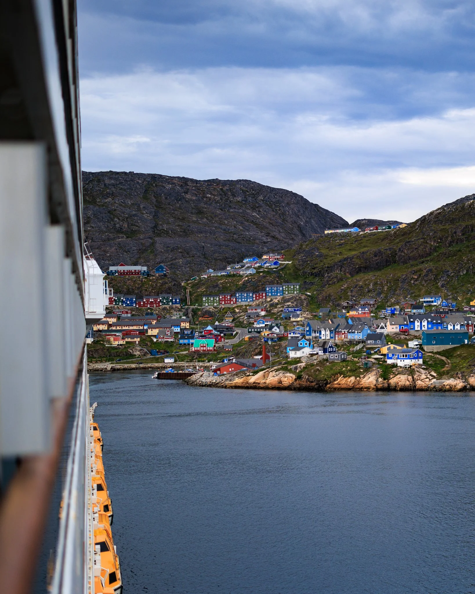 Widok z pokładu statku na kolorowe domki Qaqortoq — rozsiane na skalistym wybrzeżu tworzą charakterystyczny krajobraz tej grenlandzkiej miejscowości. Ich intensywne barwy nie są przypadkowe — dawniej pomagały odróżniać funkcje budynków i do dziś ułat
