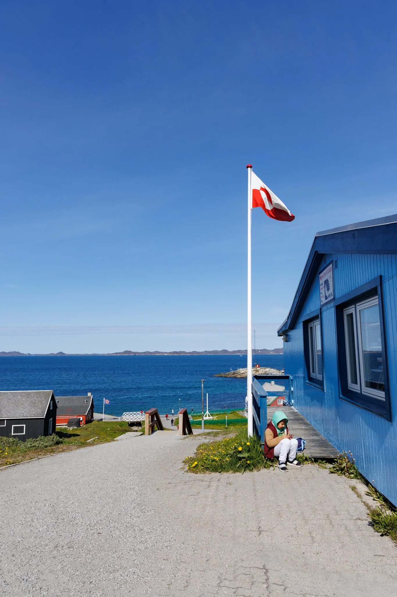 Flaga Grenlandii powiewająca na tle morza — jej czerwono-biała symbolika nawiązuje do lodu, oceanu i słońca odbijającego się w wodzie, oddając surowy charakter wyspy. To jedna z nielicznych flag regionu nordyckiego bez charakterystycznego krzyża, co 
