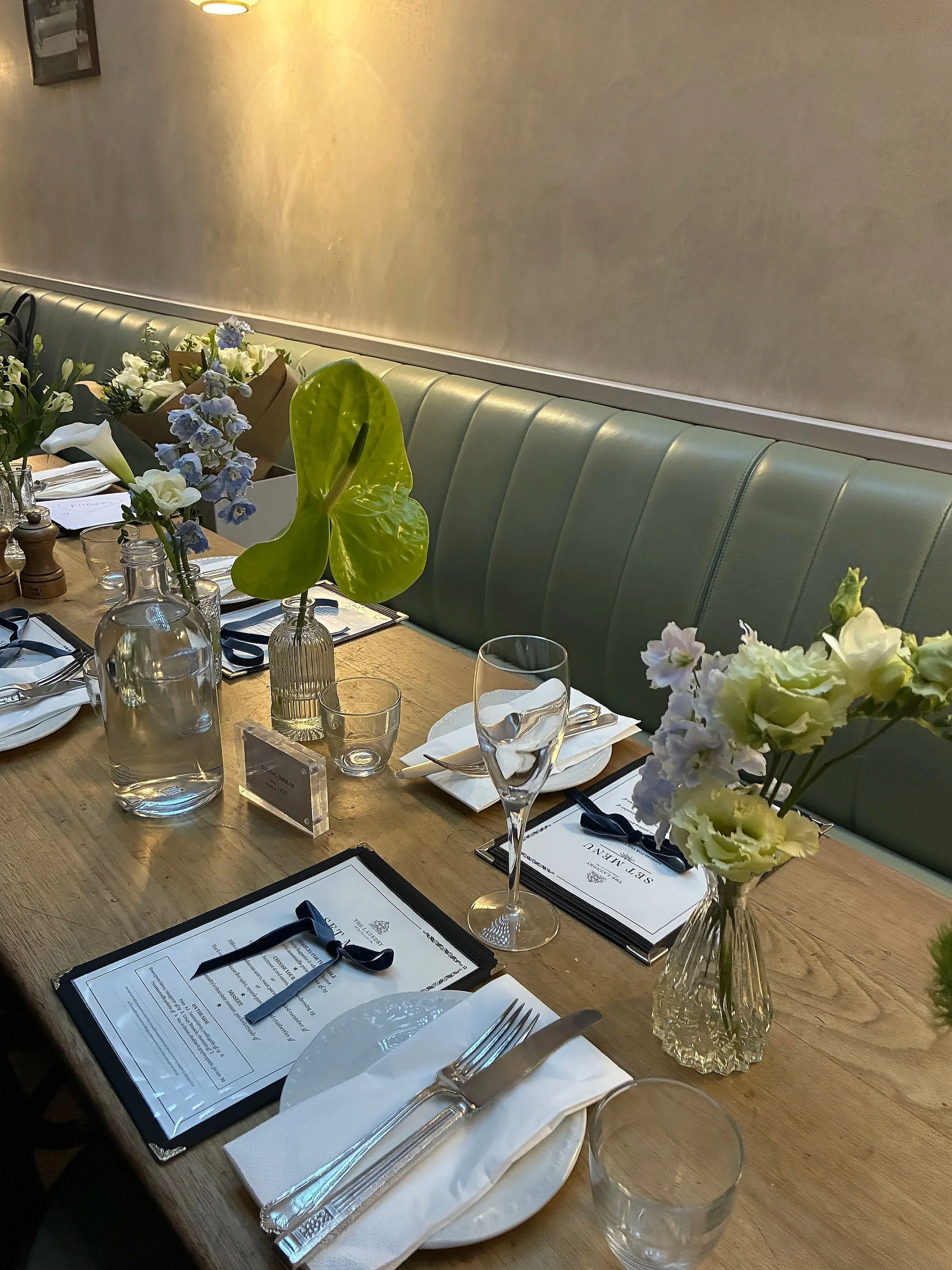 Elegant dining table set with floral centerpieces, glassware, cutlery, and menus in a softly lit restaurant setting.