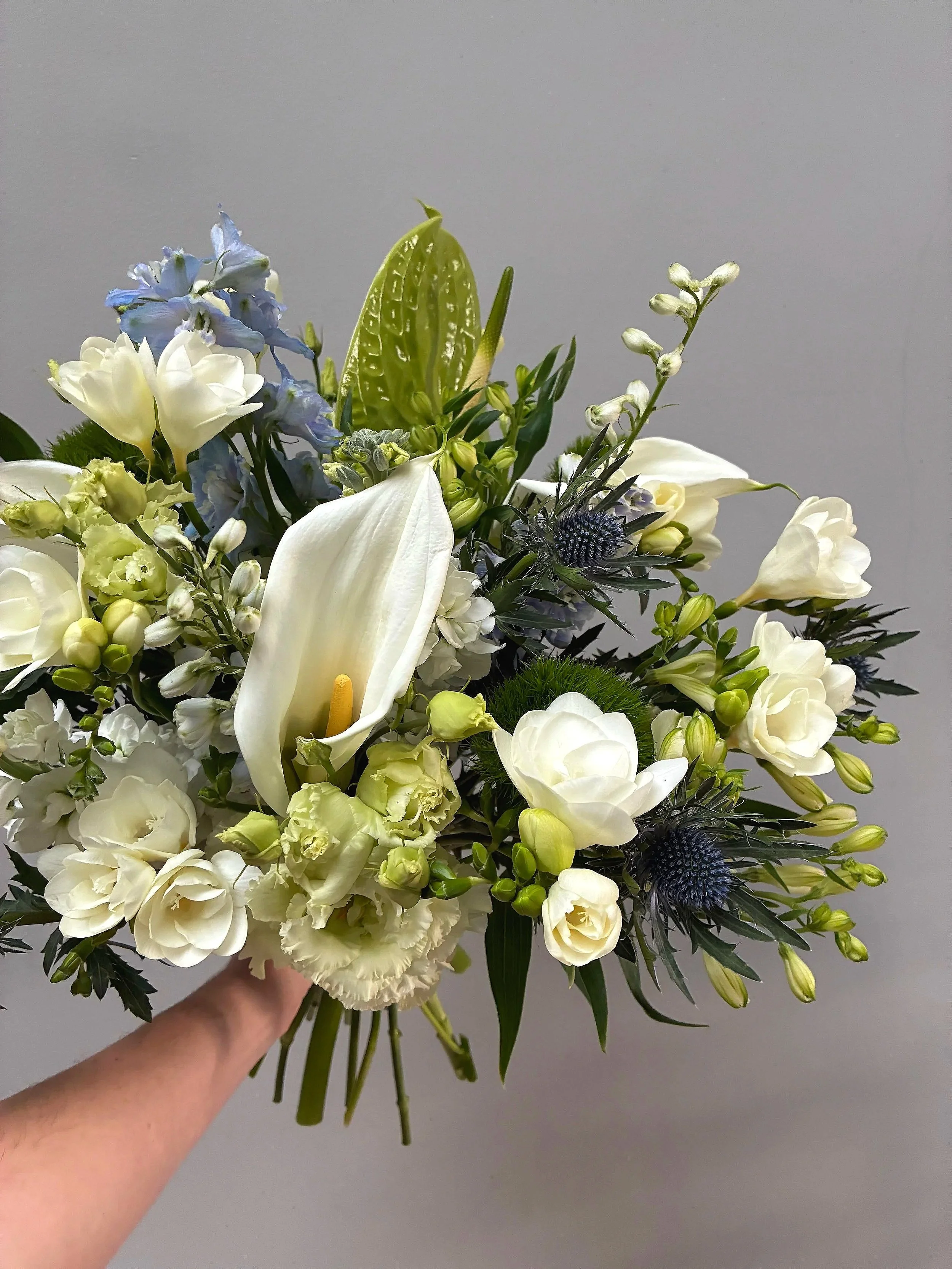 A hand holding a bouquet of white and blue flowers against a plain background.