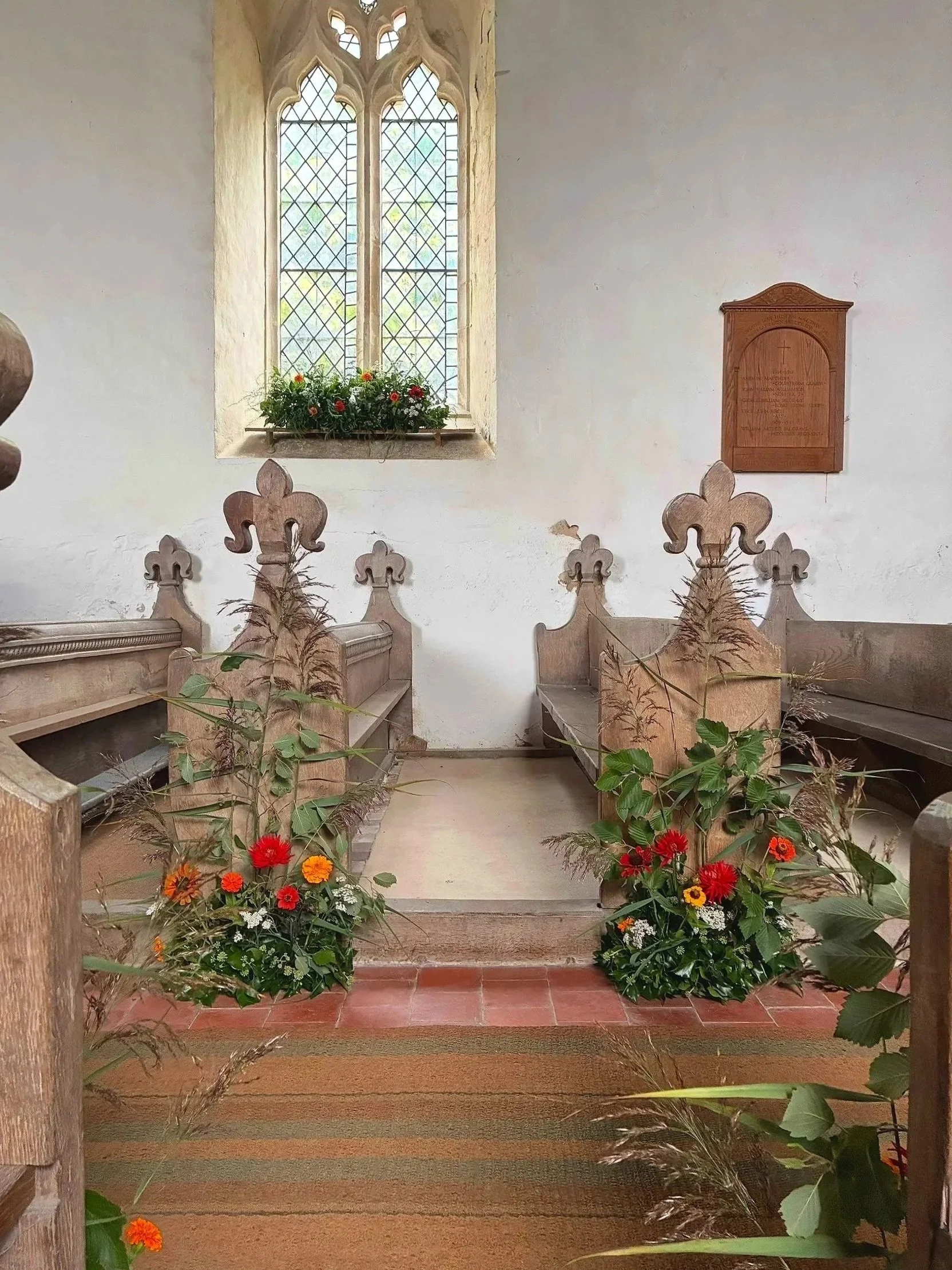 Inside a historic church with wooden pews, a stained glass window, and floral arrangements at the altar.