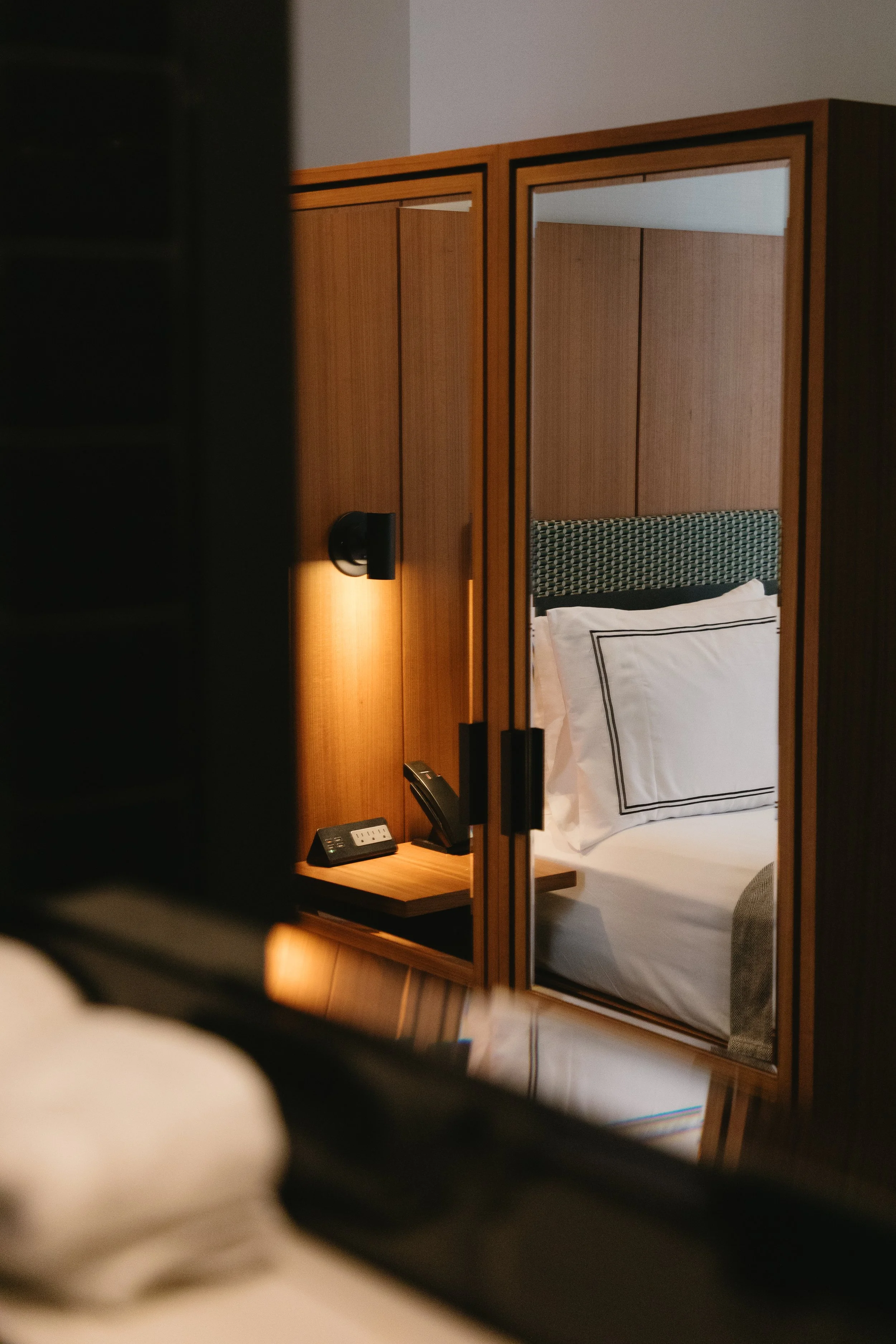 A hotel room with a bed and a mirrored wardrobe reflecting the headboard and pillows.