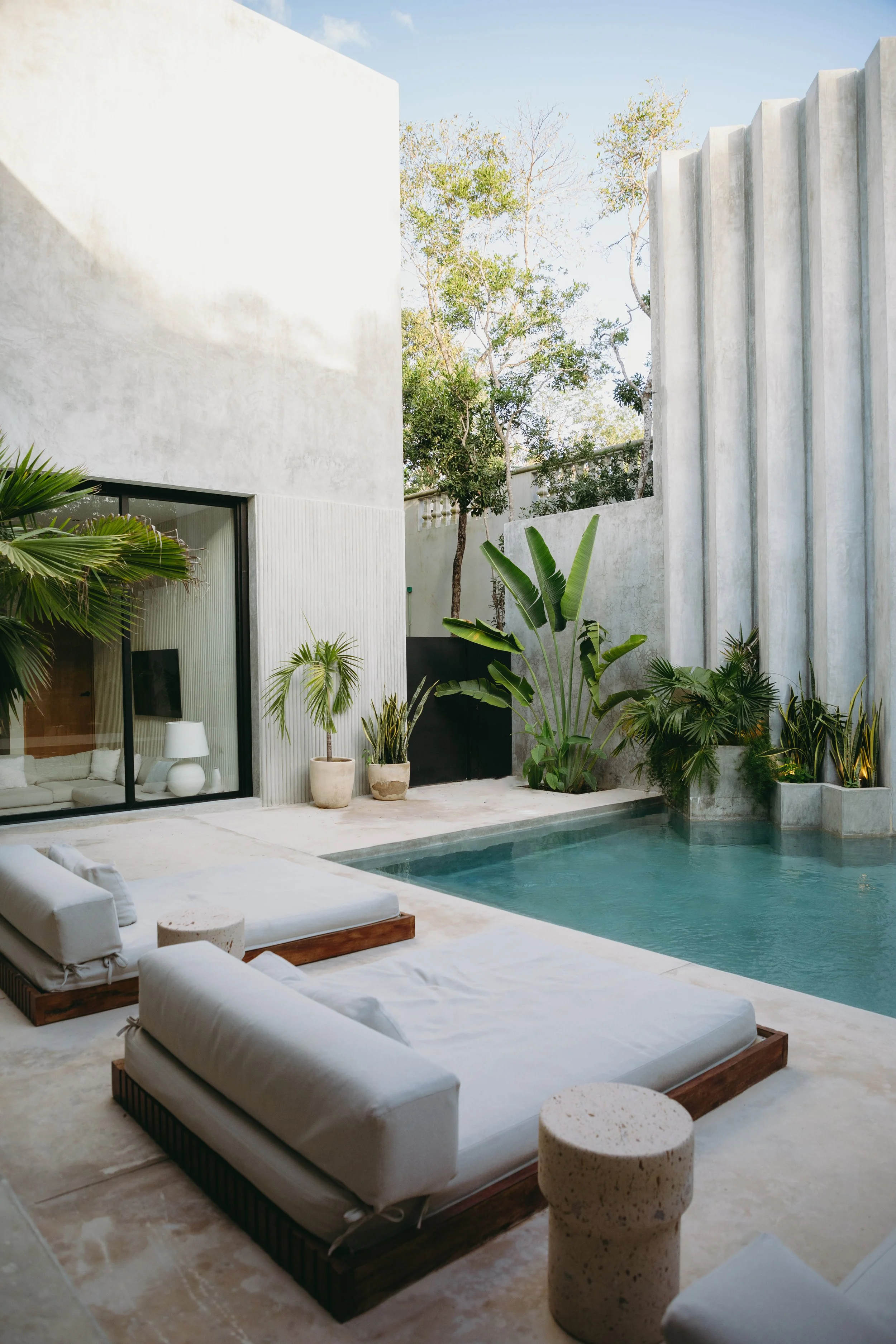 Modern outdoor pool area with white lounge chairs, potted plants, and concrete surroundings.