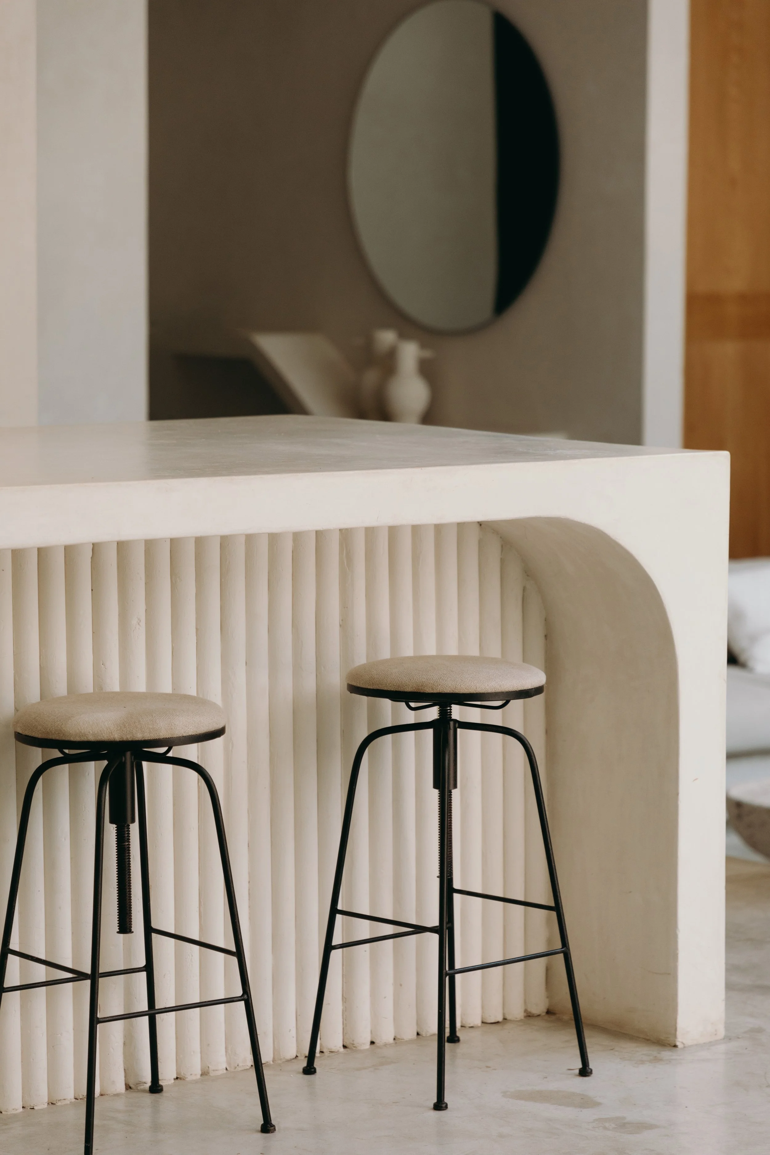 Two beige stools with black metal legs in front of a textured white bar counter in a modern interior space.