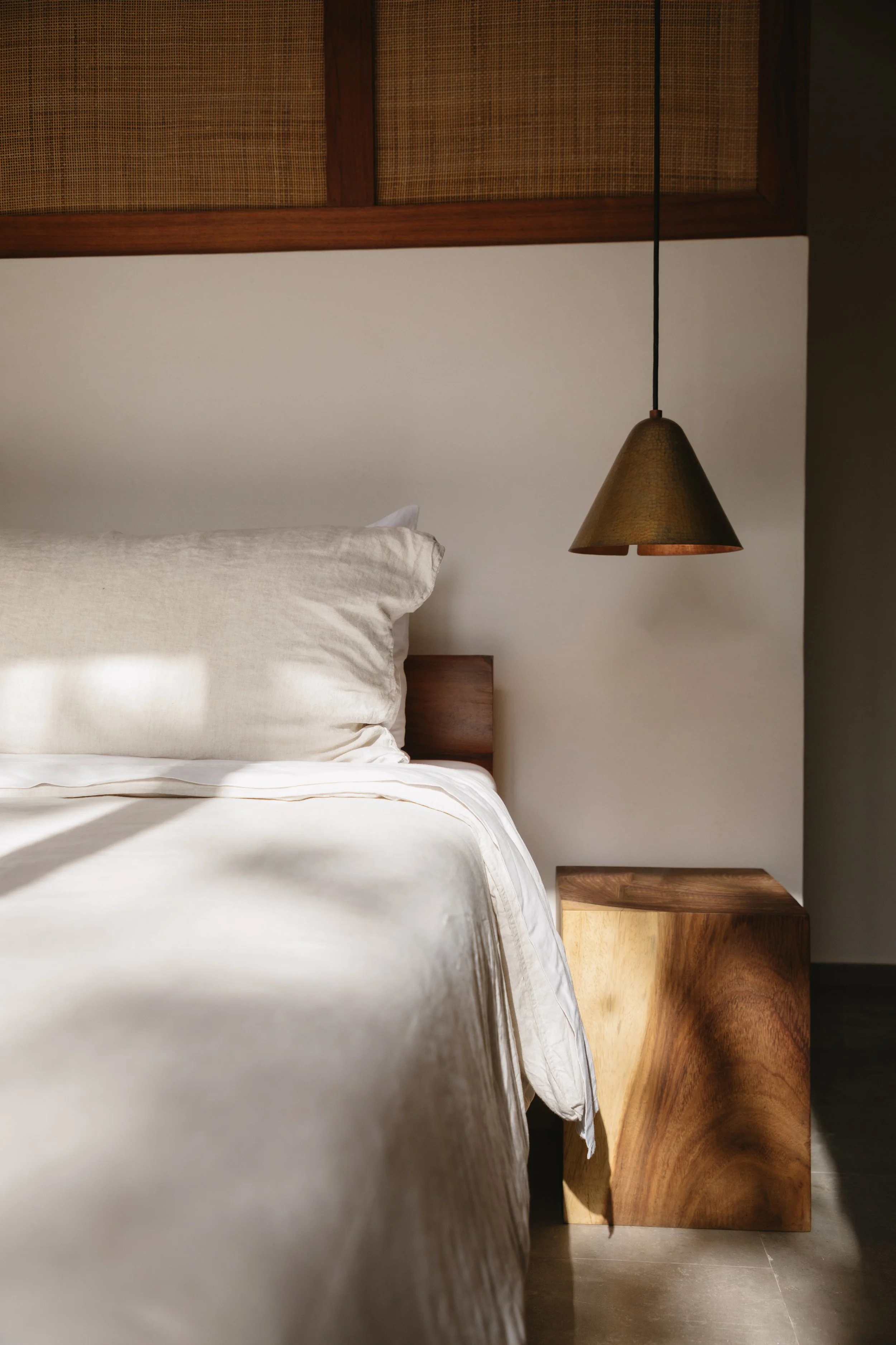 A bedroom with a bed, a pillow, a hanging pendant lamp, and a wooden nightstand.