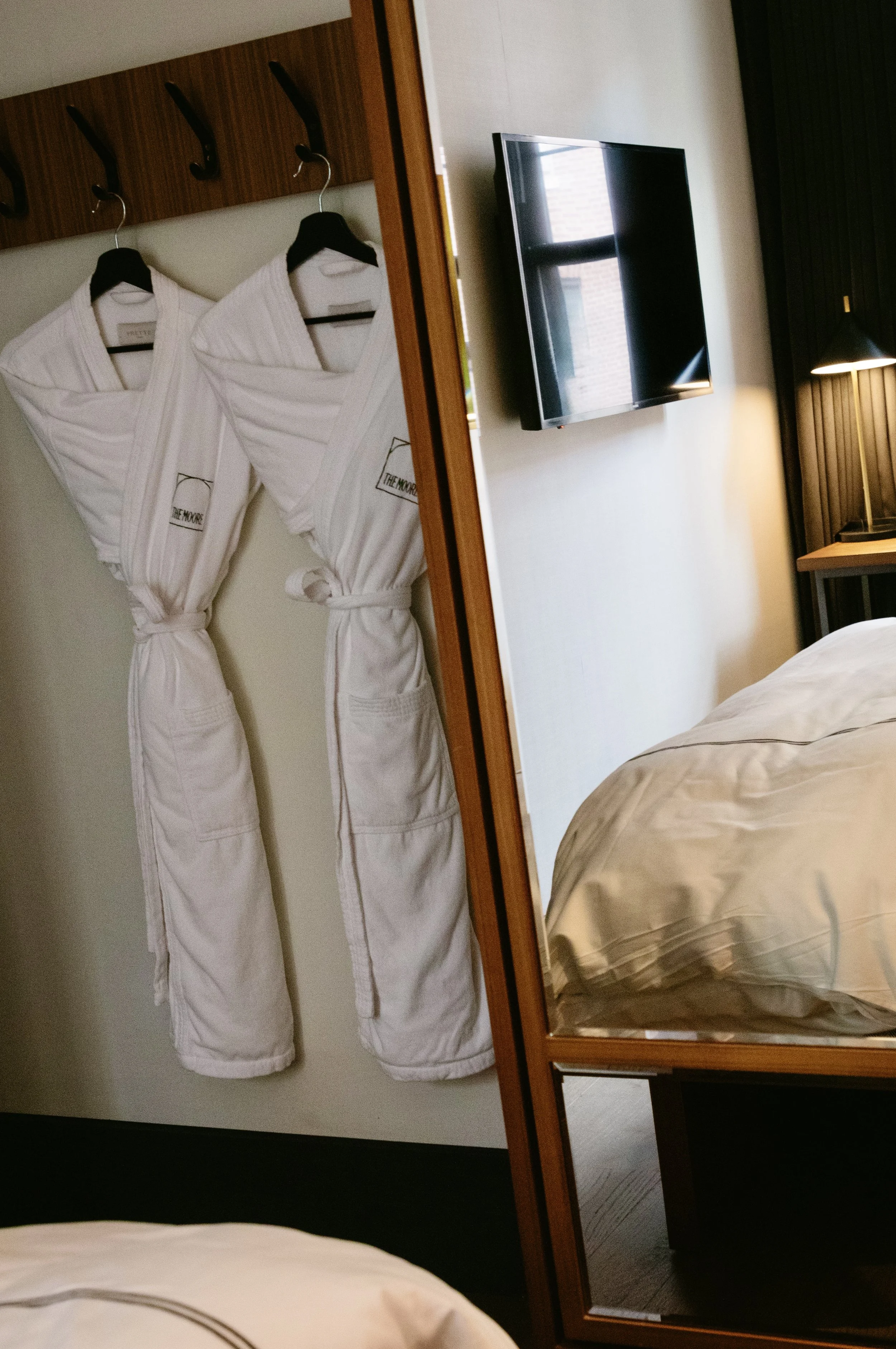 White bathrobes hanging on hooks in a hotel room, reflected in a large mirror.