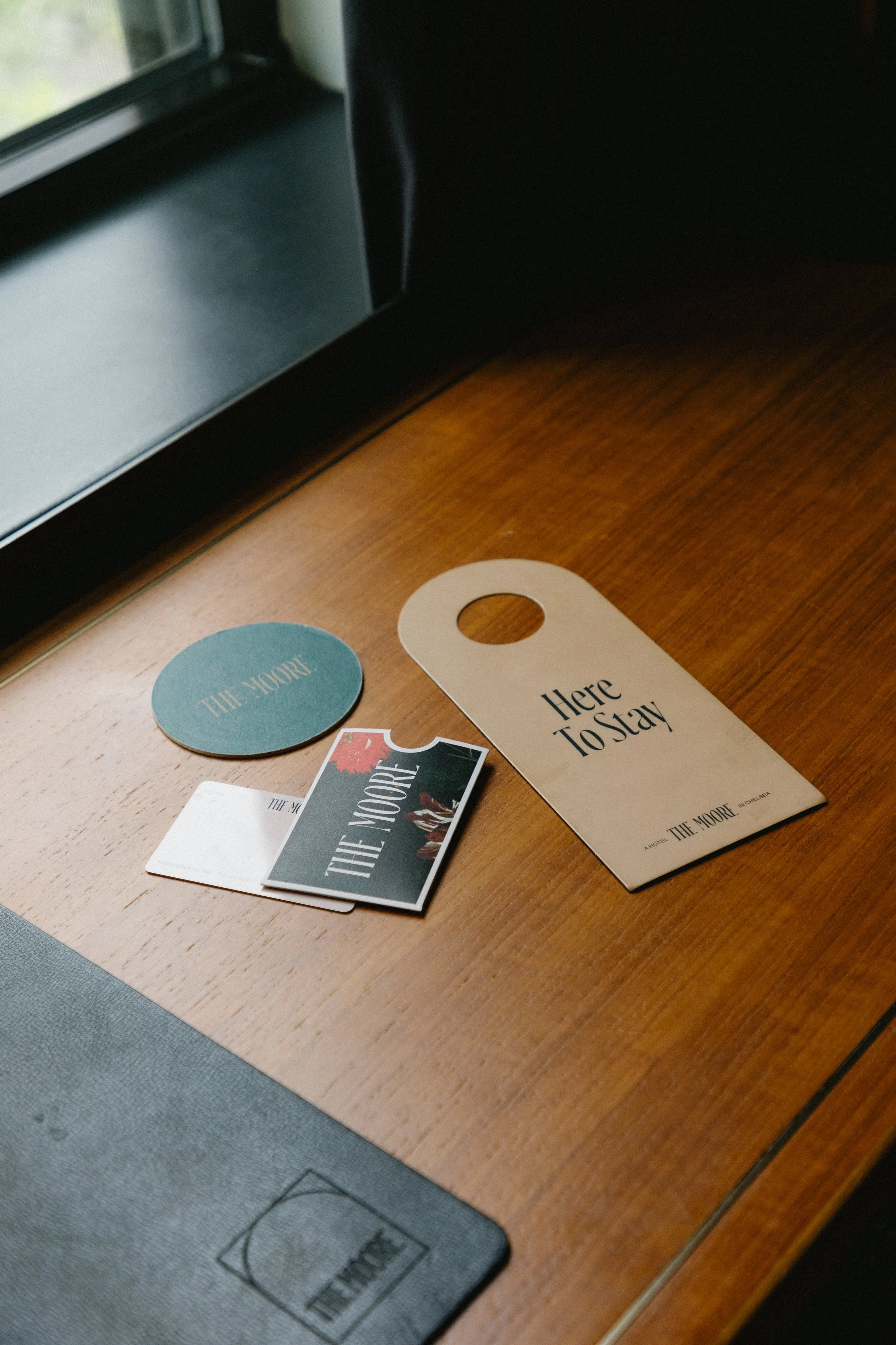 Collection of promotional tags and cards related to 'The Moore' on a wooden desk near a window.