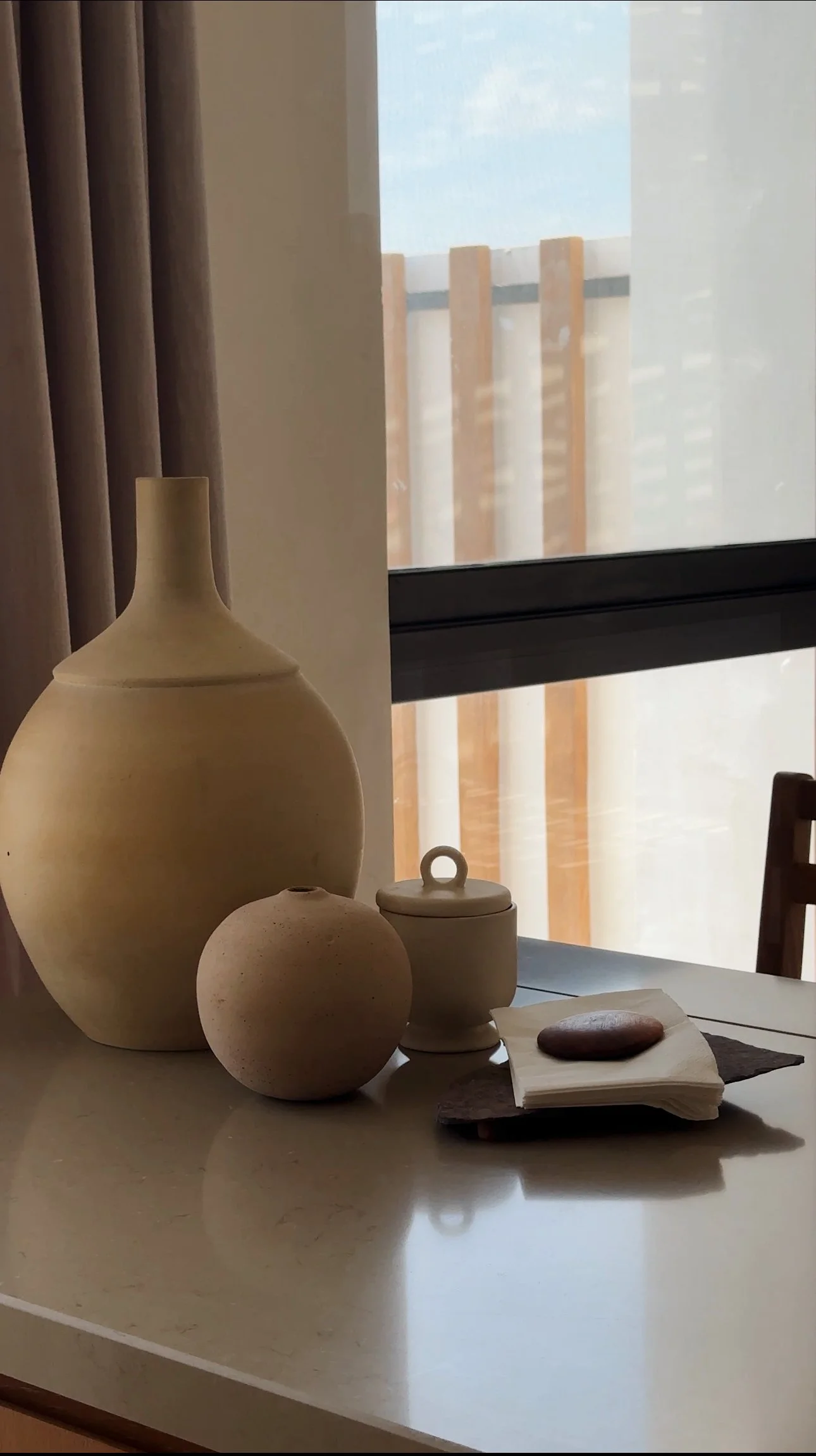 Decorative vases and a small lidded container on a table near a window with a mountain view.