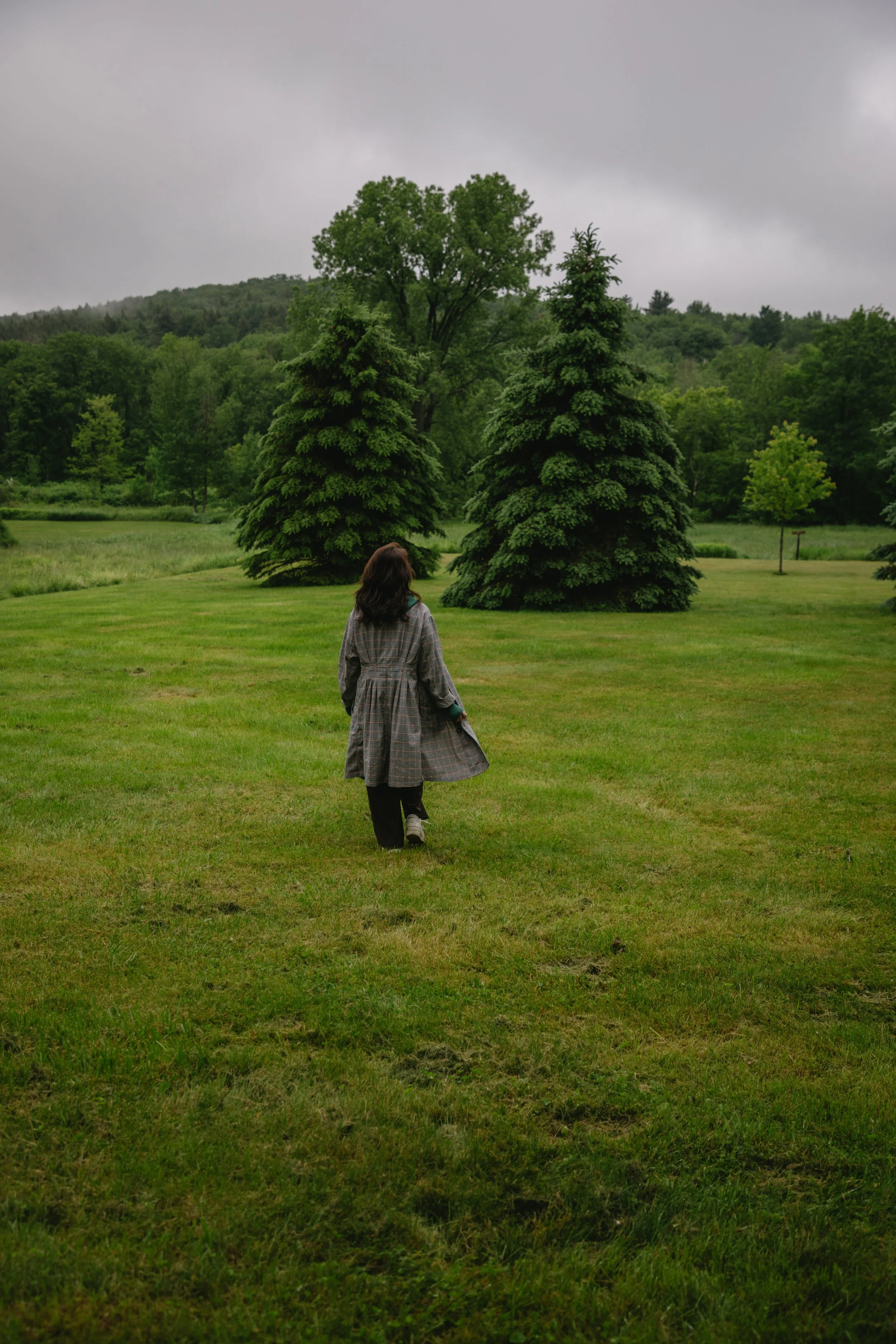 A woman walking on a grassy field with trees in the background on an overcast day.
