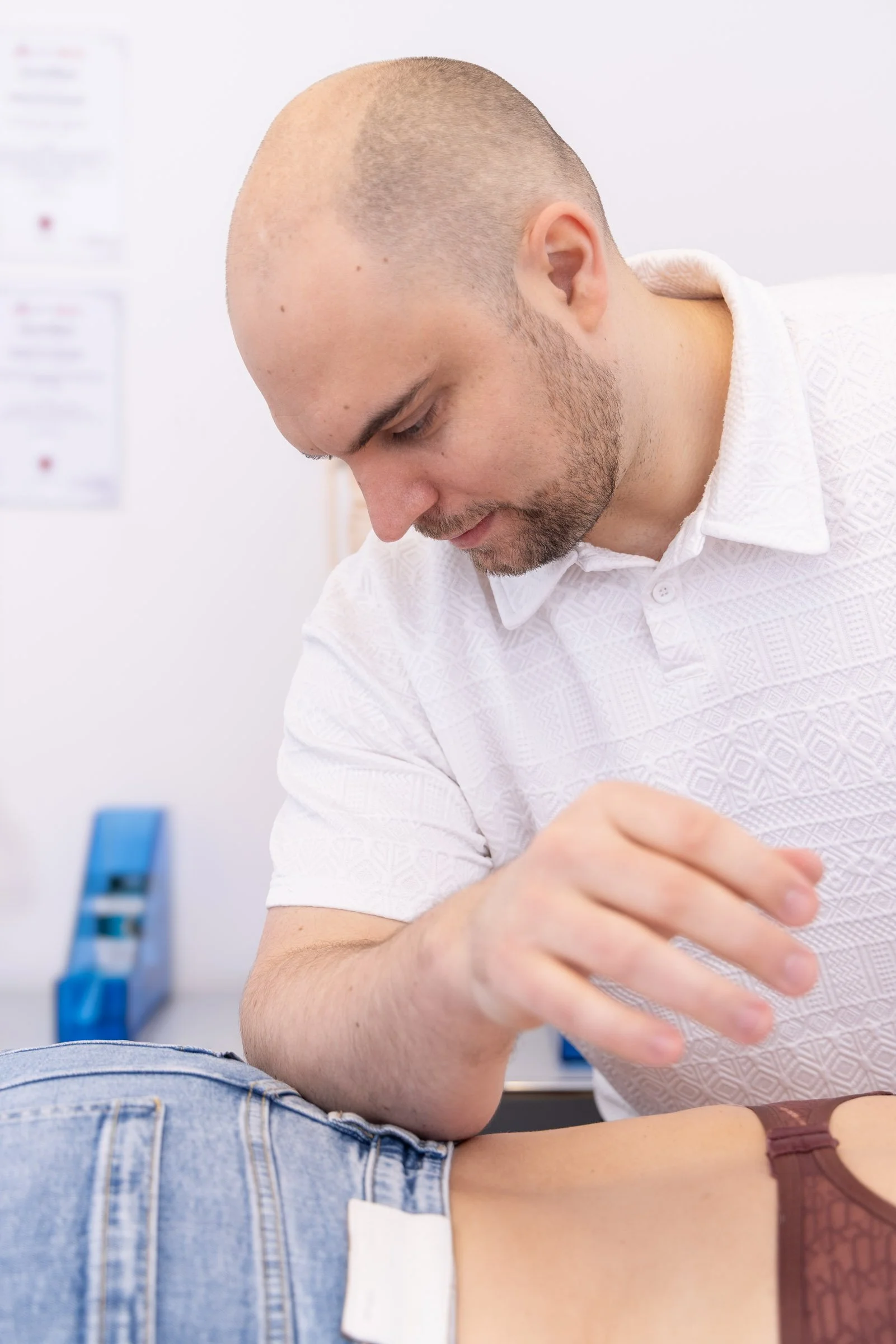 Ein Mann, der in einer Klinik oder einer Physiotherapiepraxis eine Behandlung an einer Person durchführt, die auf einer Liege liegt.