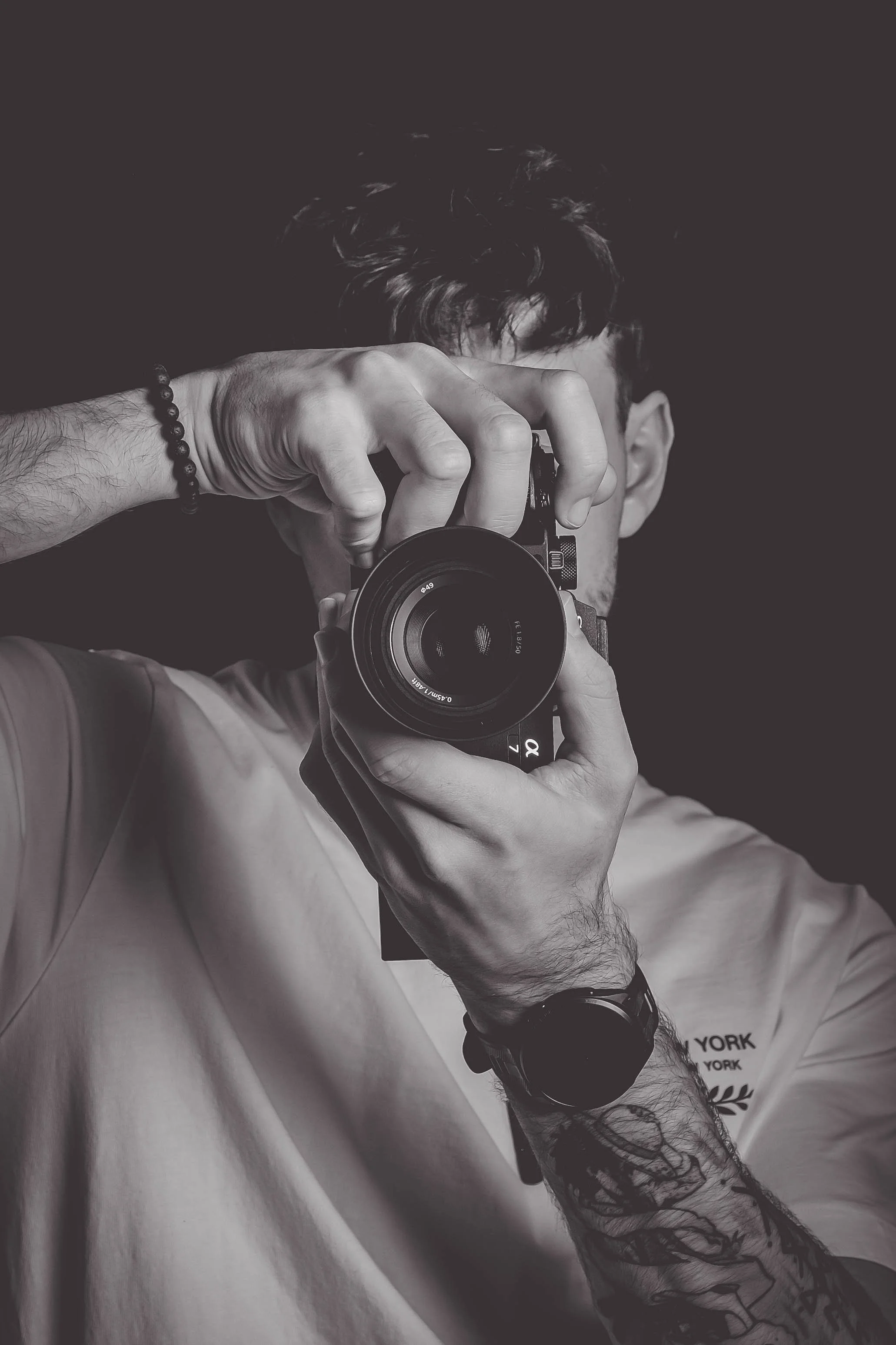 Un homme tenant un appareil photo, prenant un autoportrait en noir et blanc dans un studio.