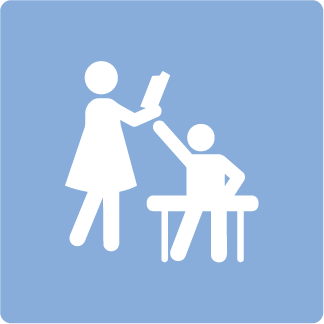 A teacher raising a book to a student who is sitting at a desk.