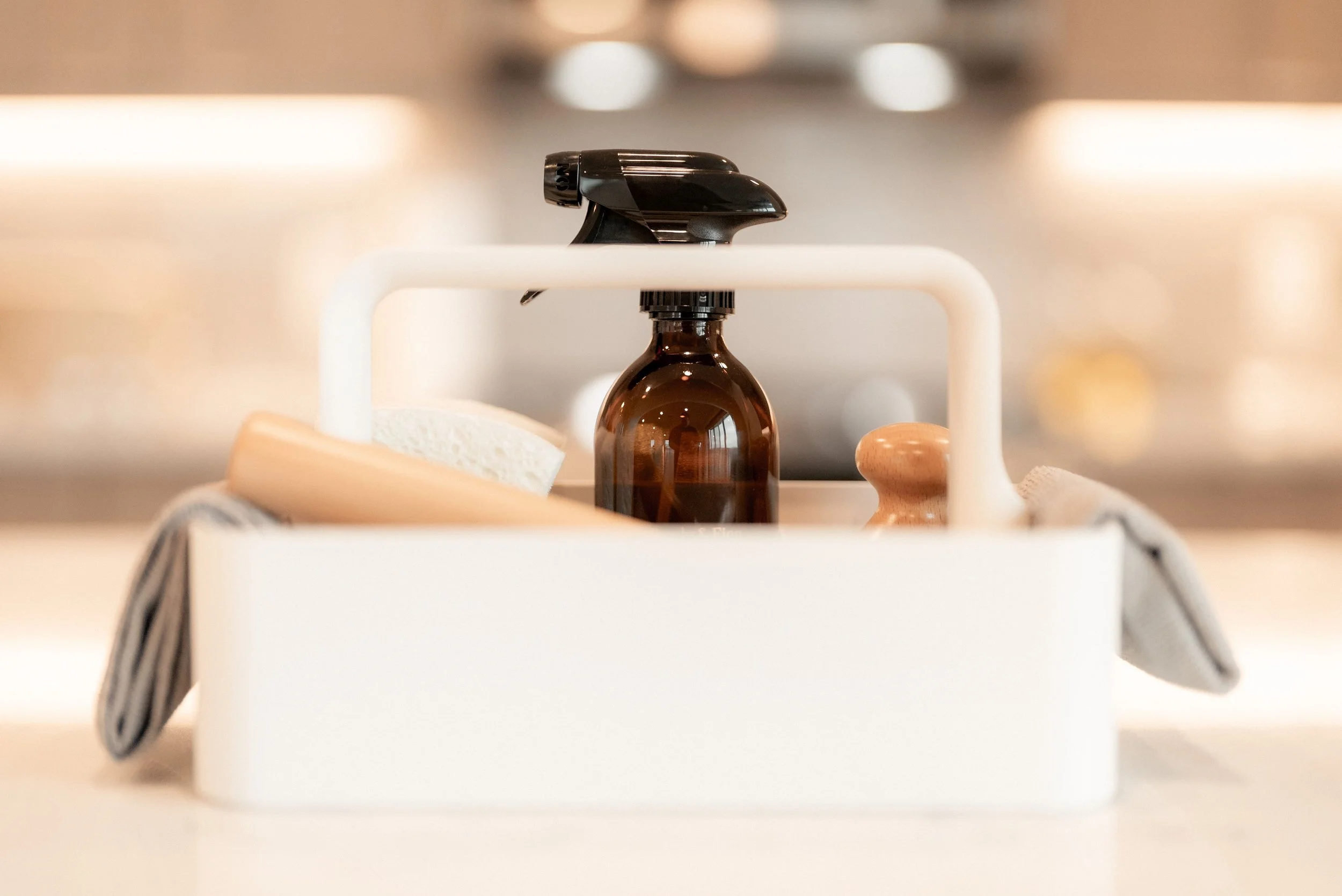Kitchen sink organizer with a brown spray bottle, a scrub brush, a sponge, and dish towel.