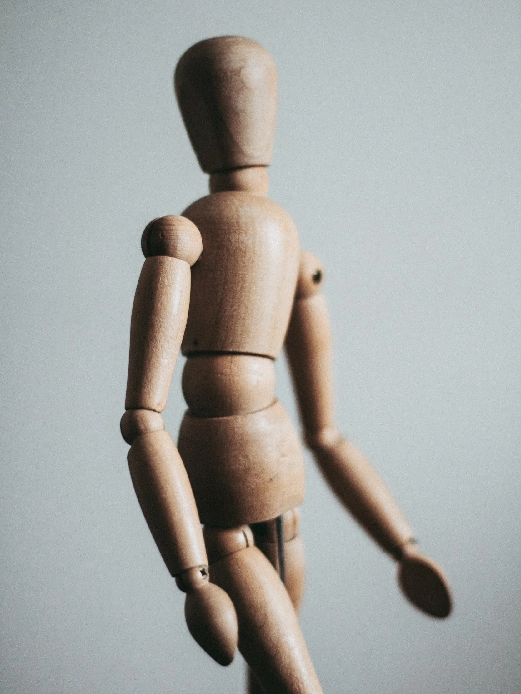 A close-up of a wooden artist mannequin with a plain light gray background.