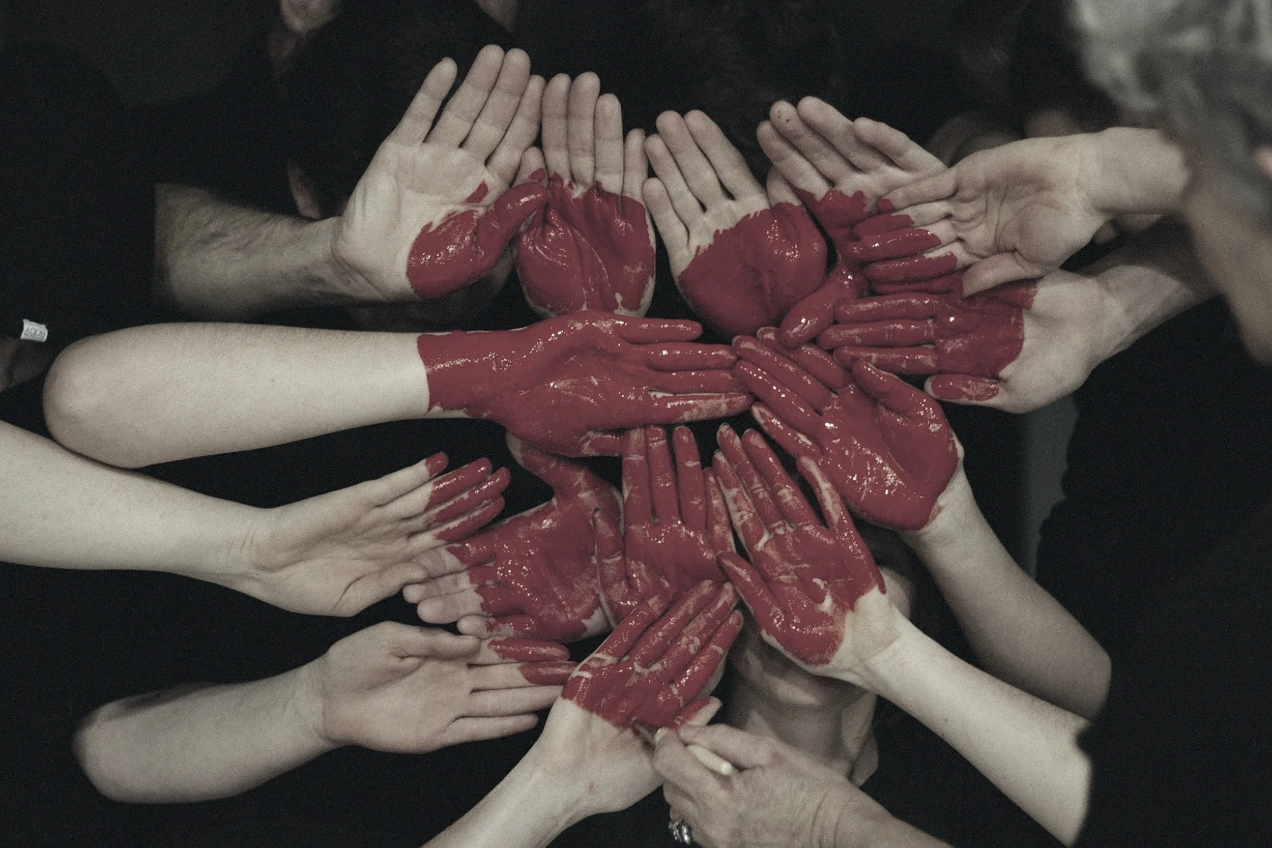 Multiple hands with painted red hands and fingers forming a heart shape.
