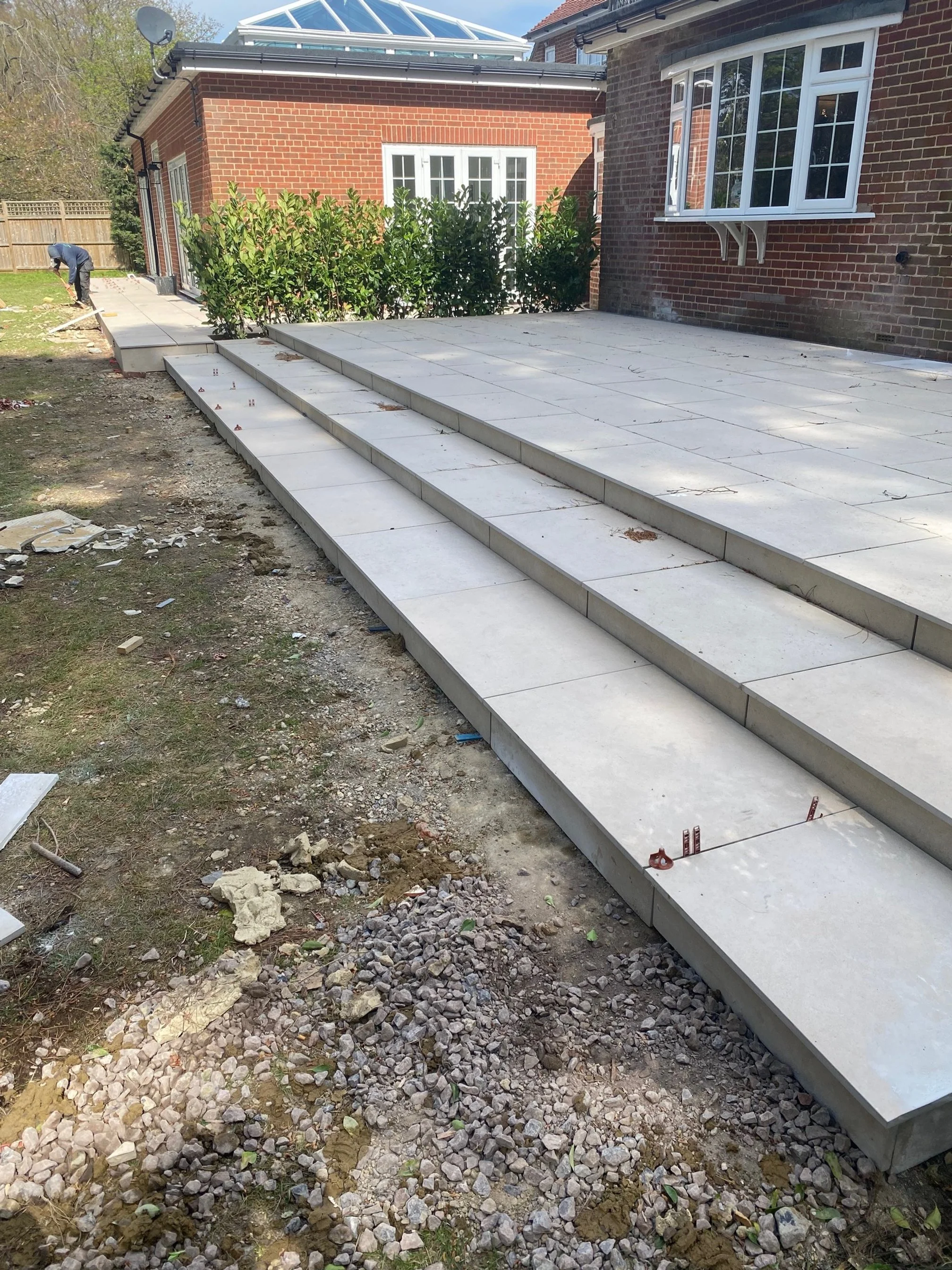 Construction workers installing large stone or concrete slabs on a new outdoor patio with steps leading up to the house in the backyard.