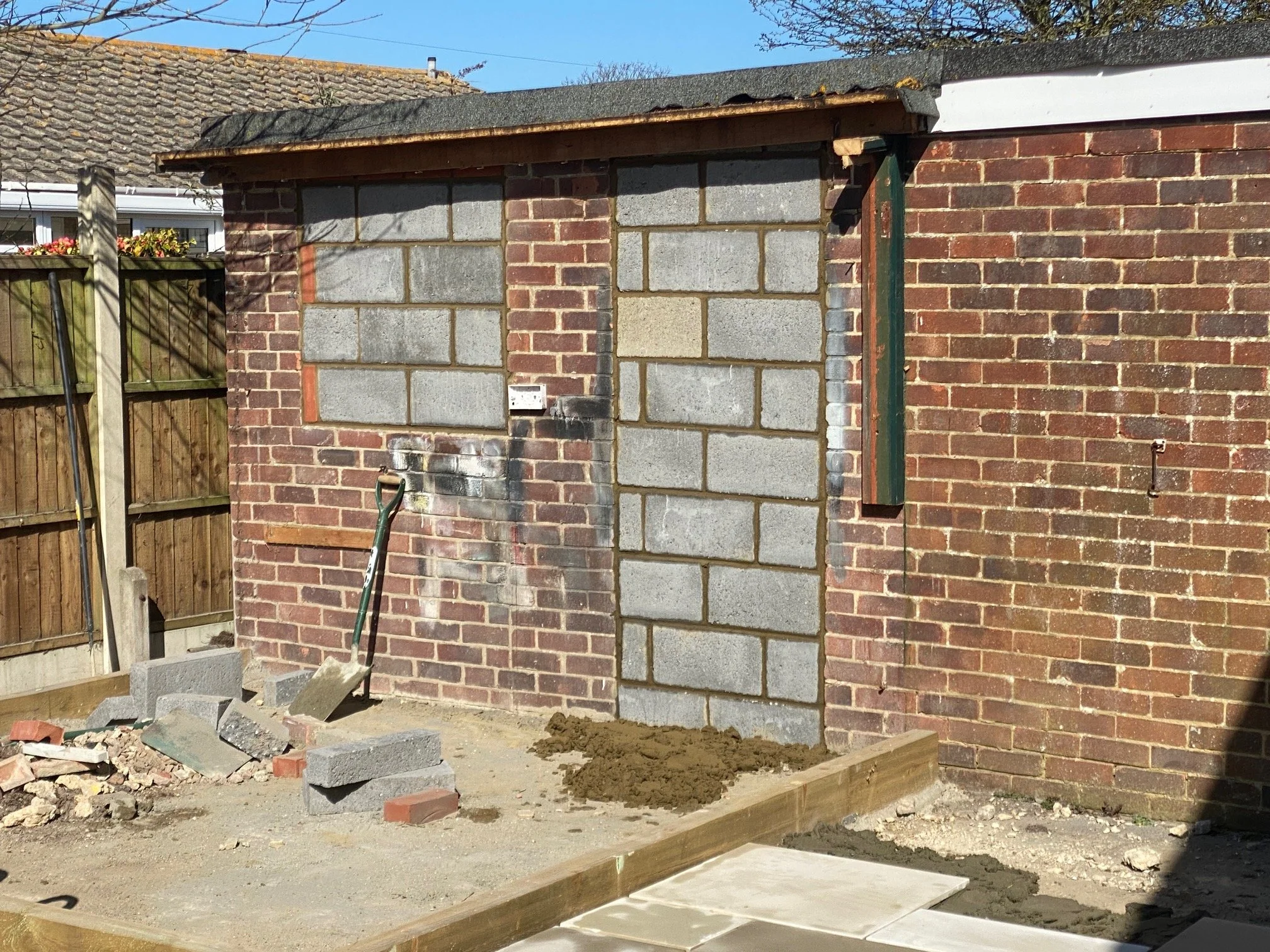 Construction site in backyard with bricks, cement blocks, soil, and wooden framing for a building extension.